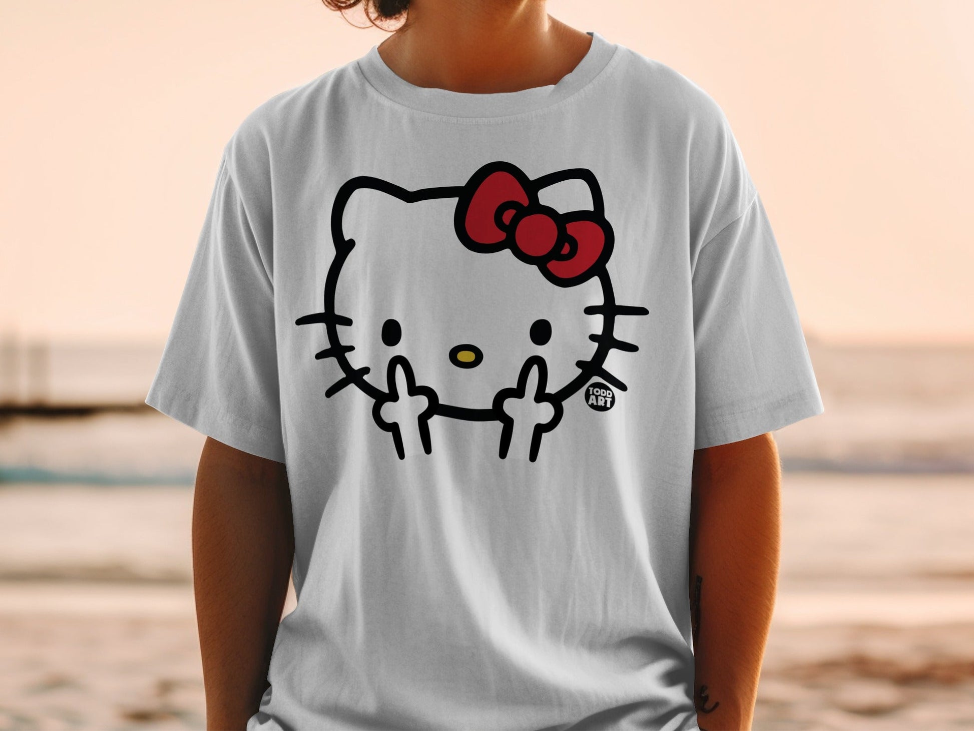 White t-shirt with Hello Kitty giving middle fingers, "1000 ART" logo.