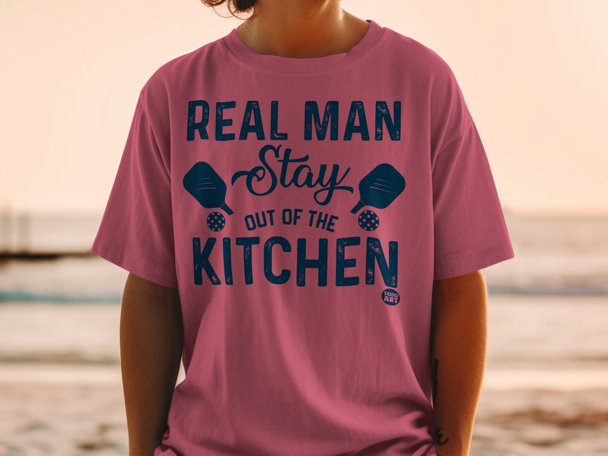 Pink t-shirt with blue text and pickleball paddles.
