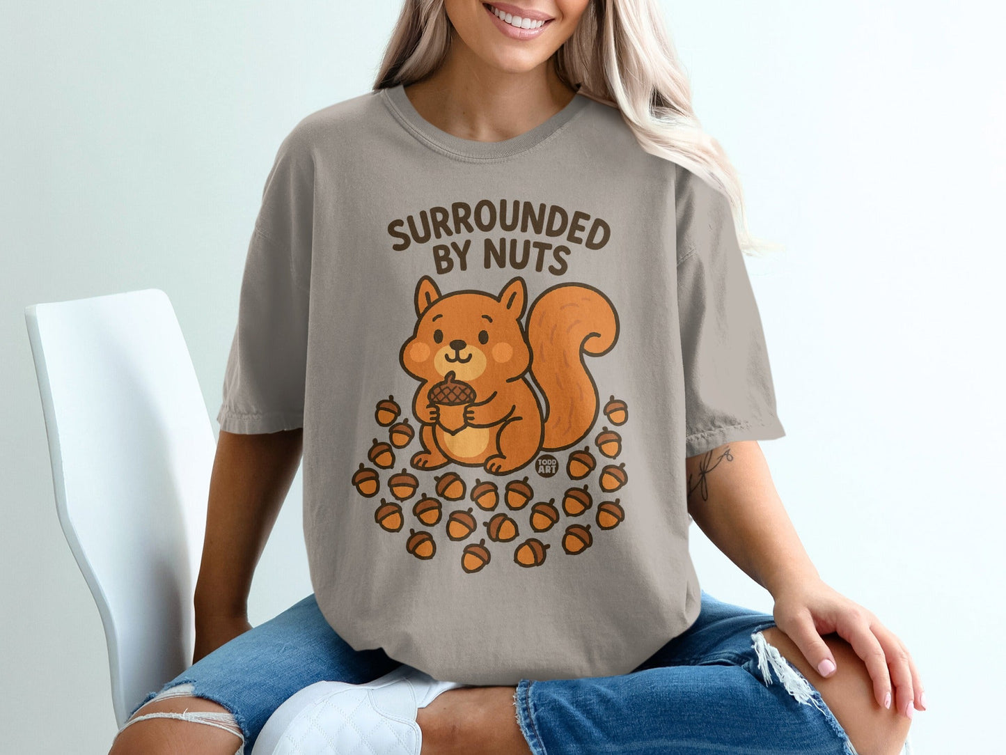 T-shirt with a cartoon squirrel holding an acorn surrounded by nuts.