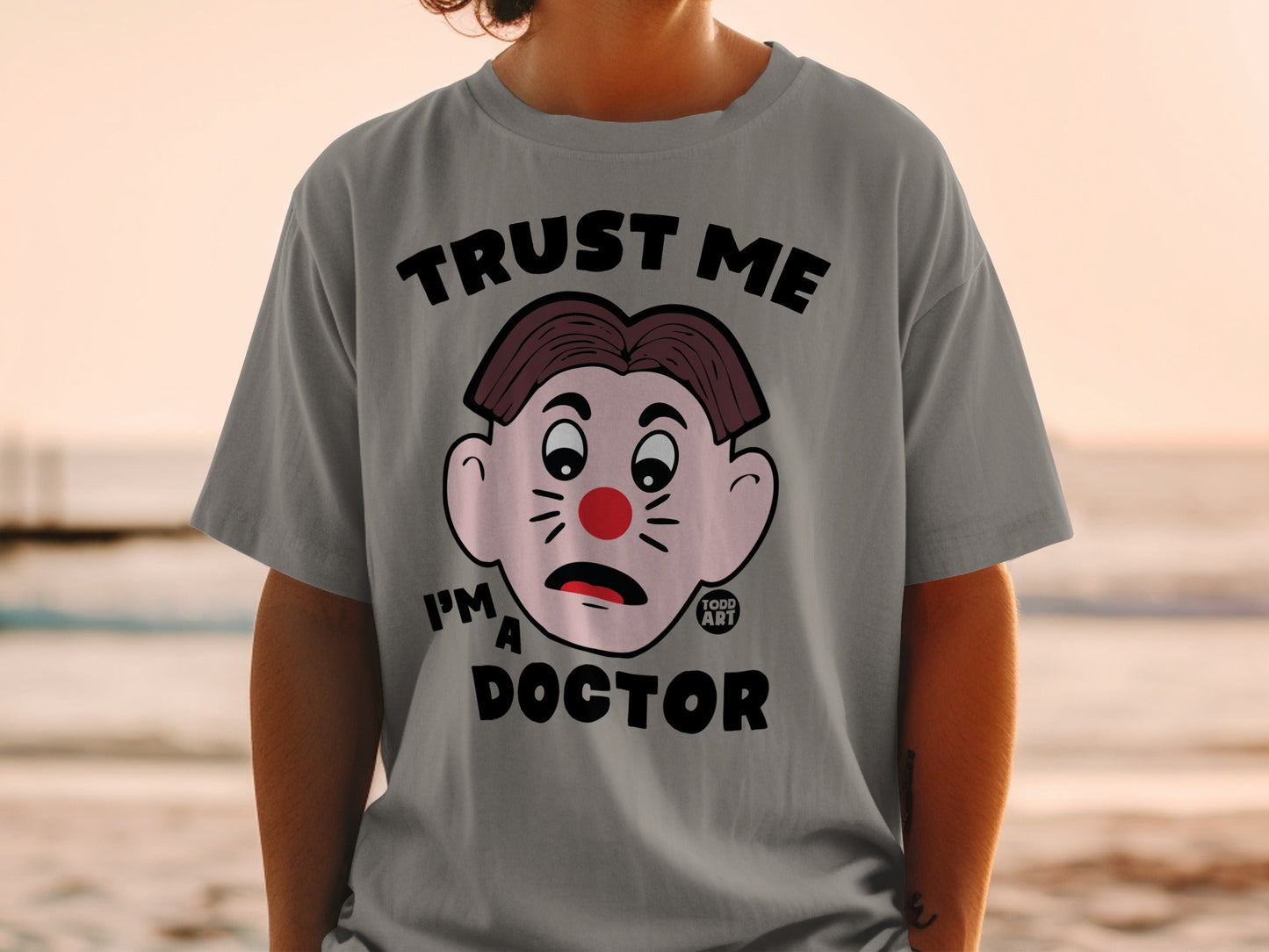 Grey t-shirt with cartoon face and "TRUST ME I'M A DOCTOR" text.