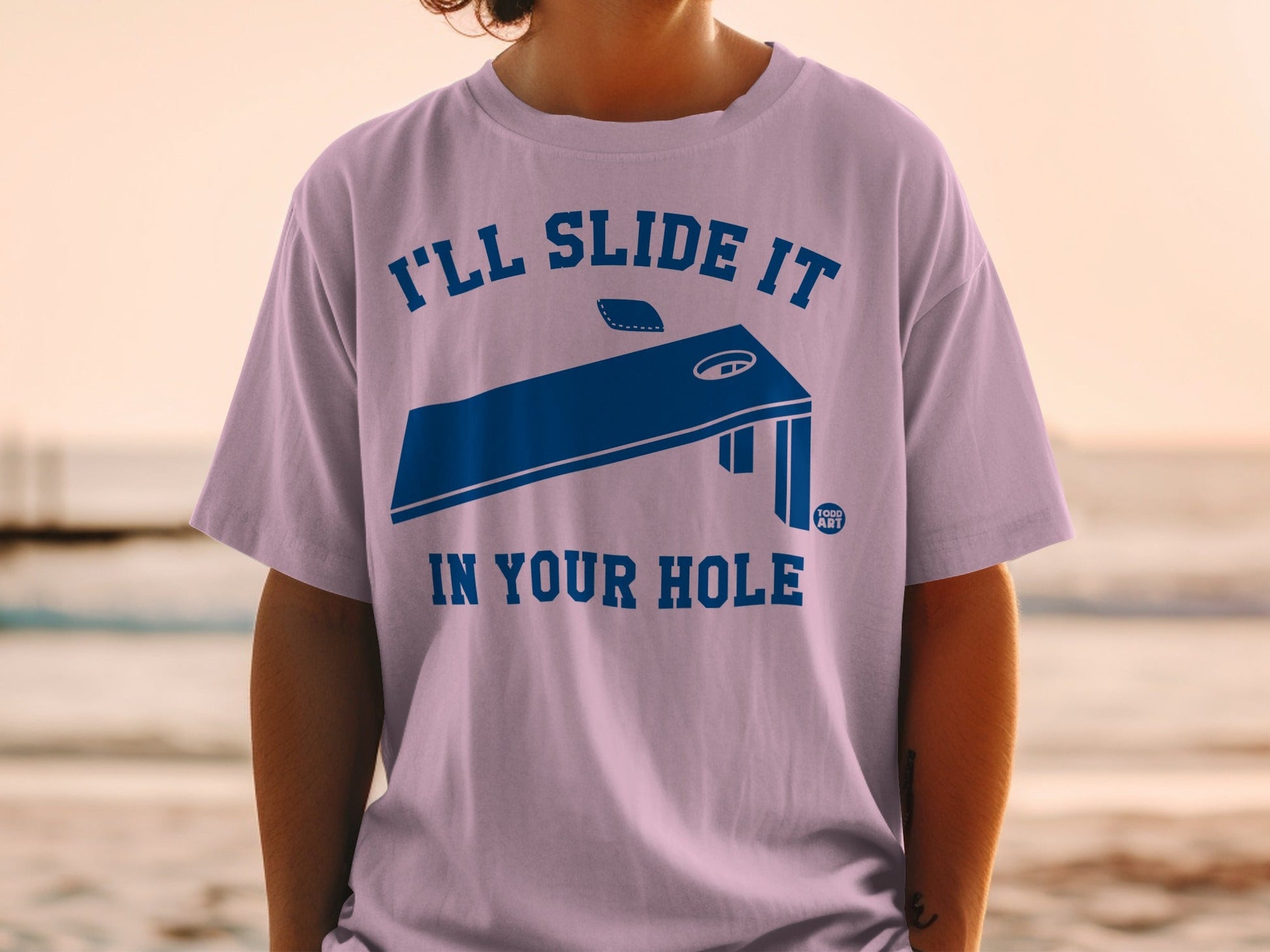 Purple t-shirt with "I'LL SLIDE IT IN YOUR HOLE" text and cornhole board graphic.