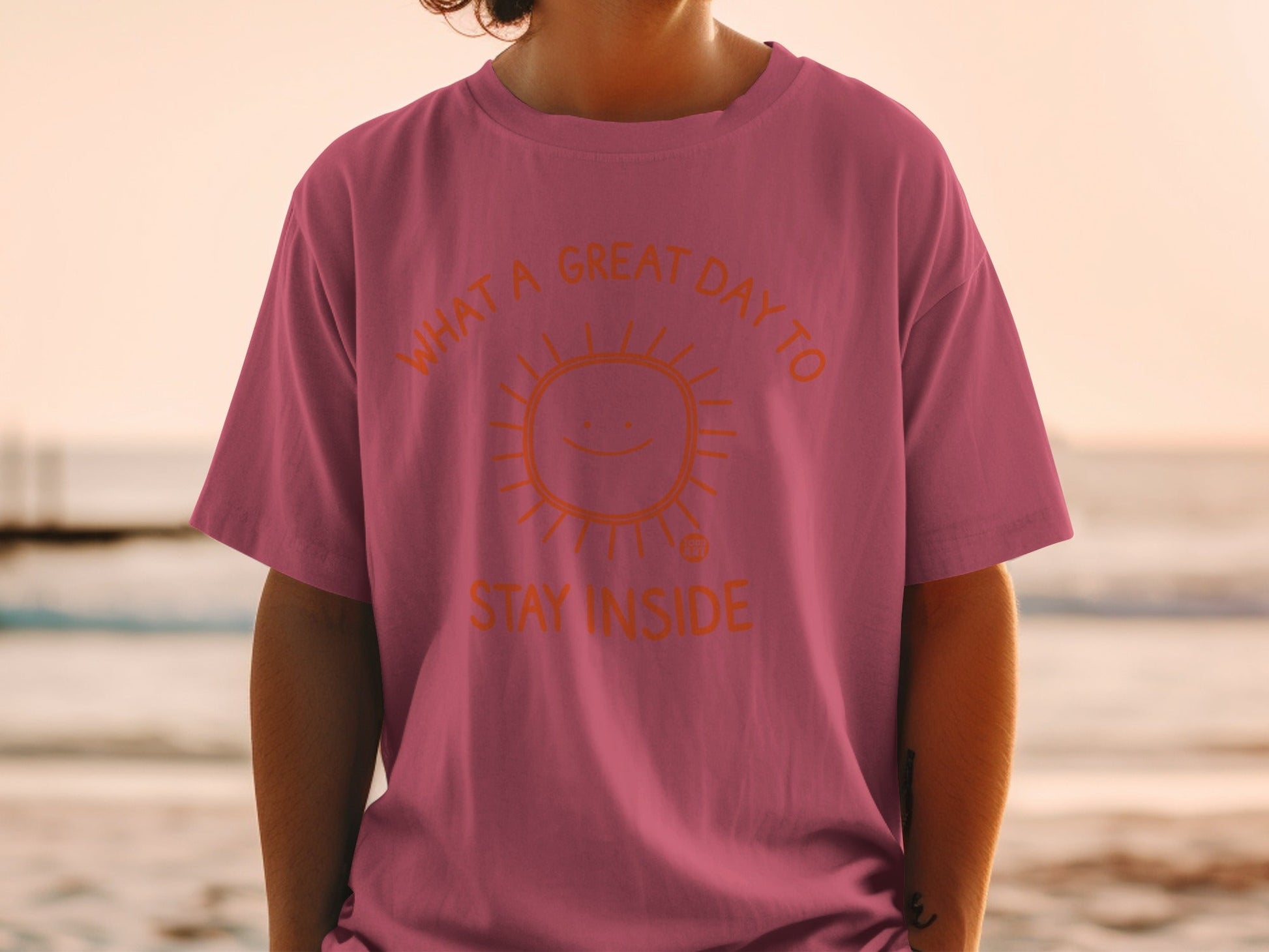 Pink t-shirt with orange text and sun graphic that reads "What a great day to stay inside."