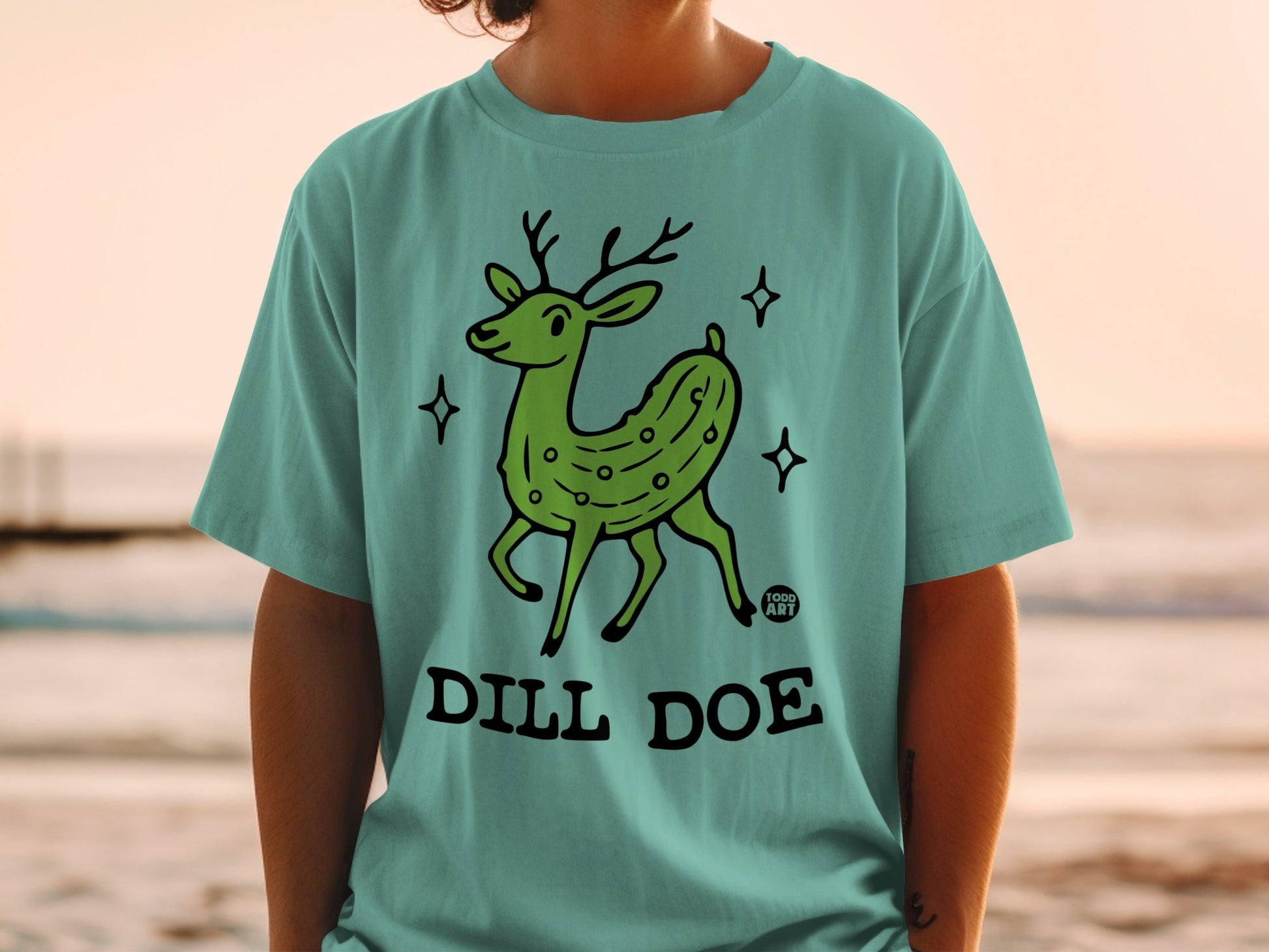 Green cartoon deer with pickle pattern on teal t-shirt, "Dill Doe" text.