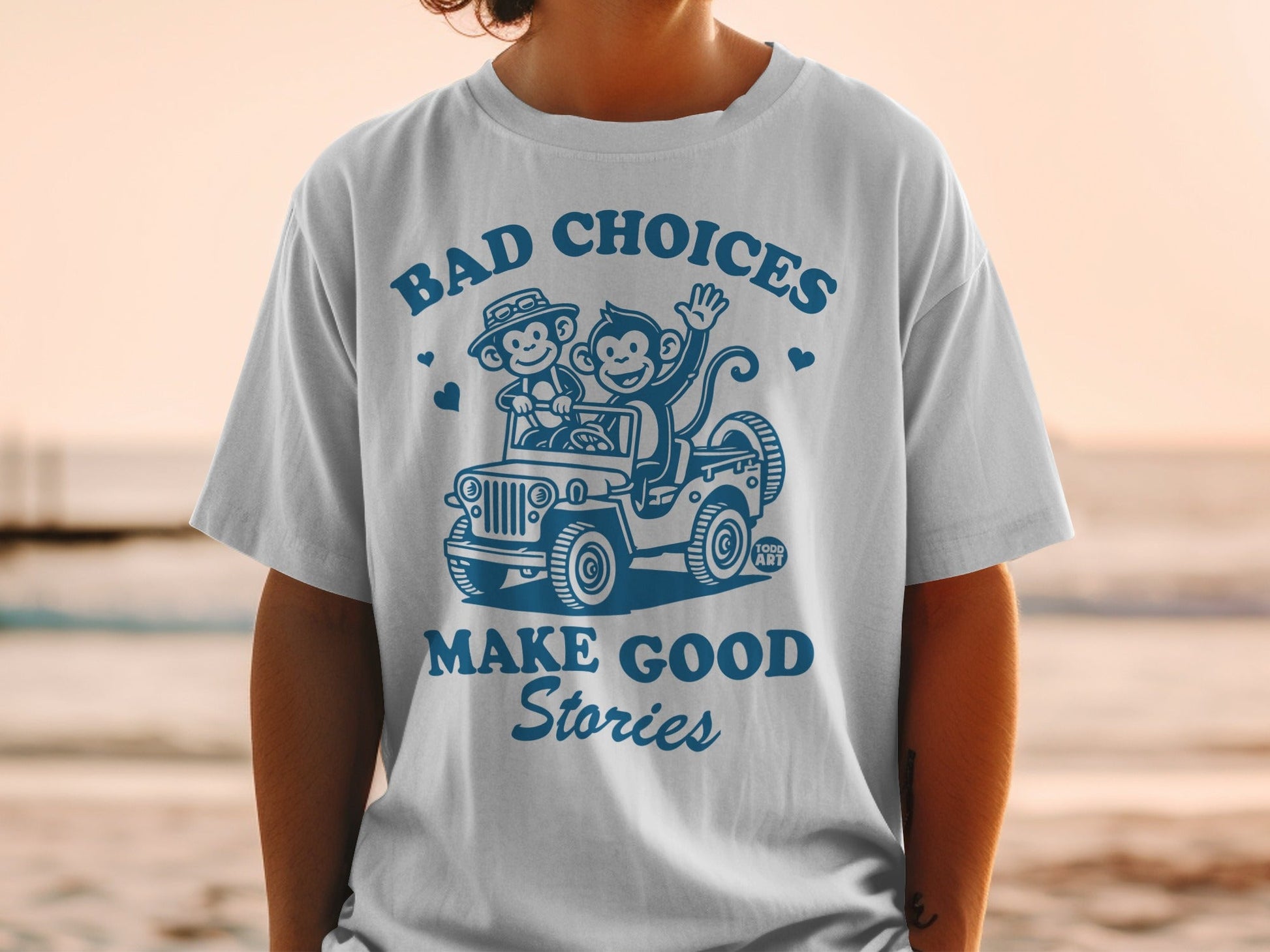 White t-shirt with blue graphic of monkeys in a jeep, "Bad Choices Make Good Stories".