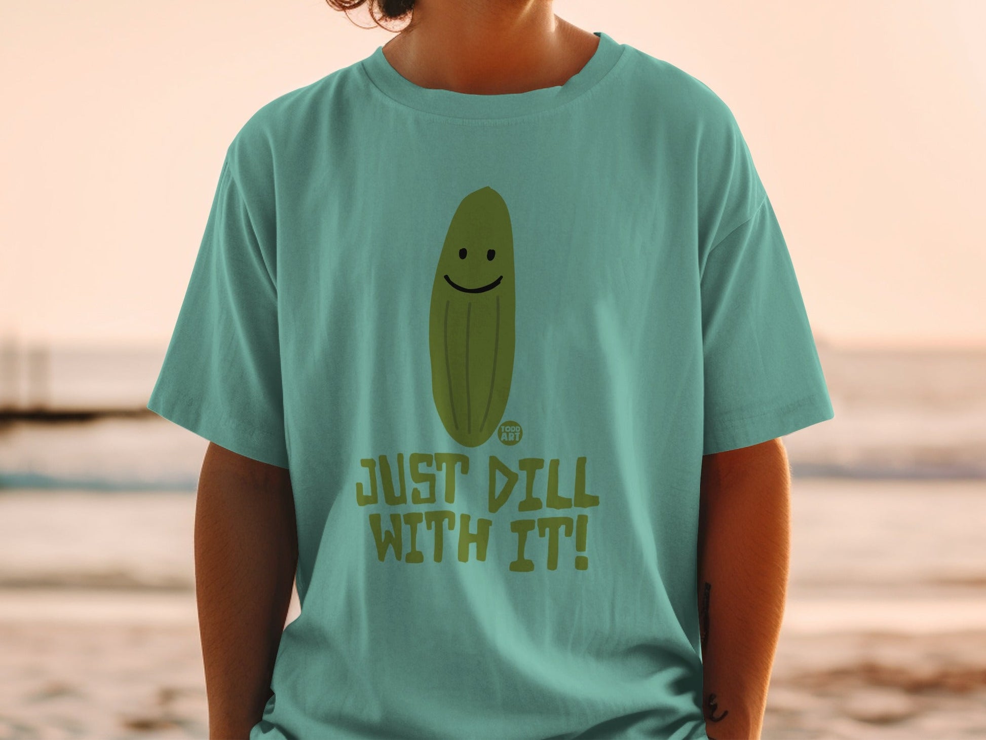 Green t-shirt with smiling pickle and text "JUST DILL WITH IT!".