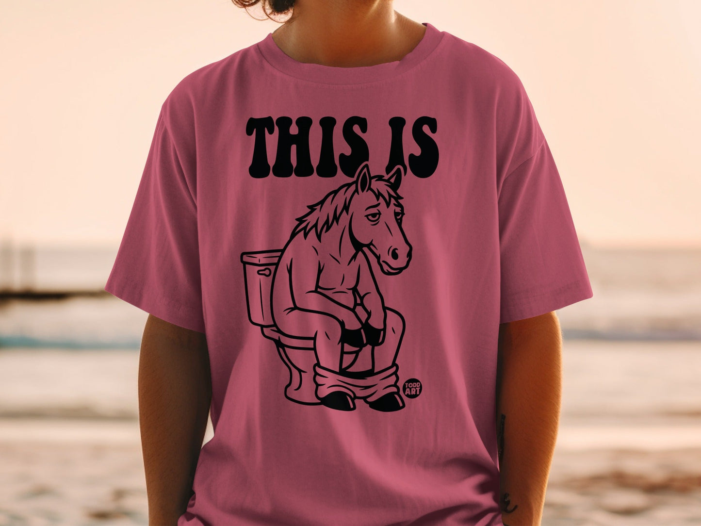 Pink t-shirt with black graphic of a horse sitting on a toilet.