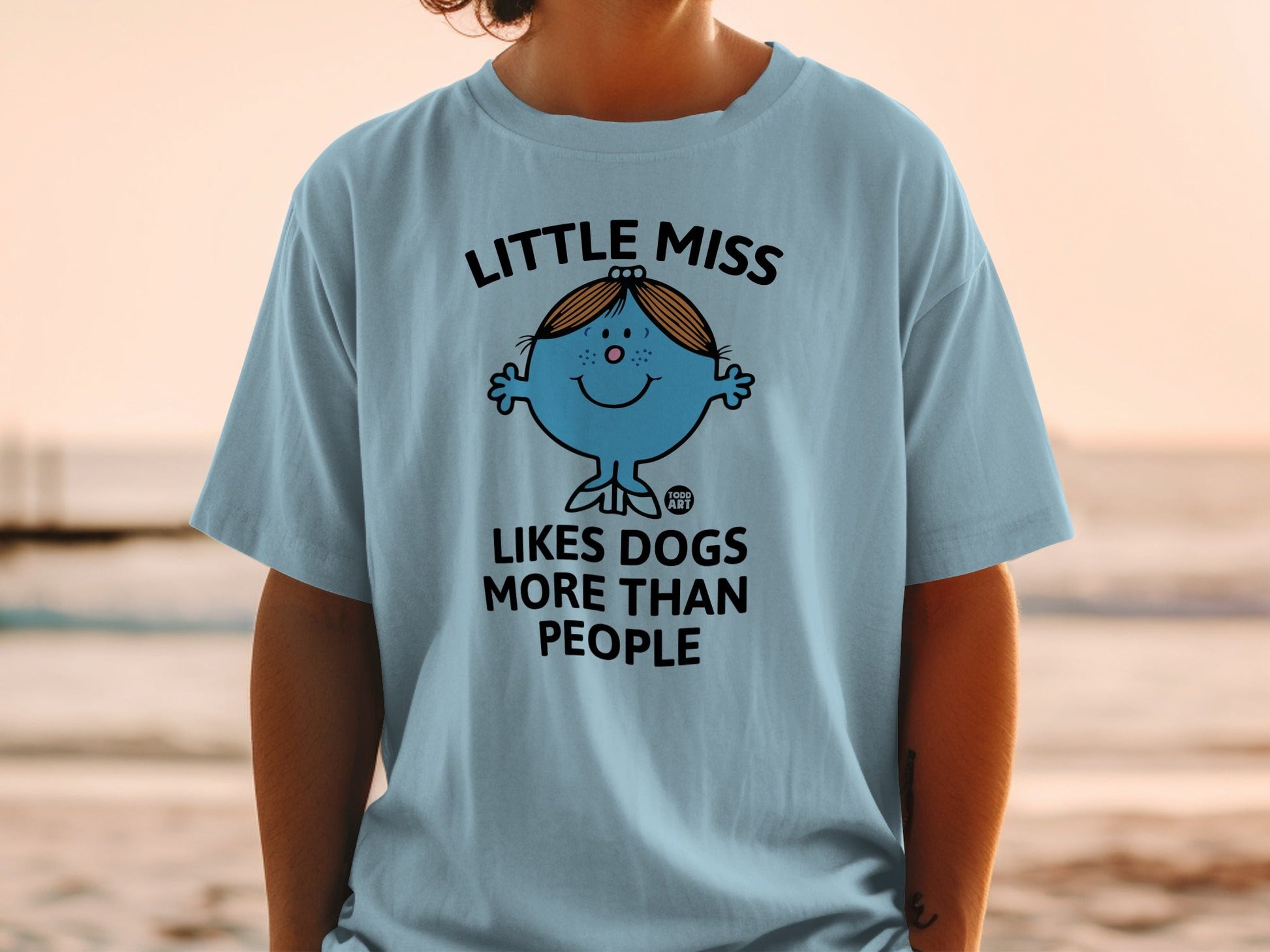 Light blue t-shirt with "Little Miss Likes Dogs More Than People" graphic.