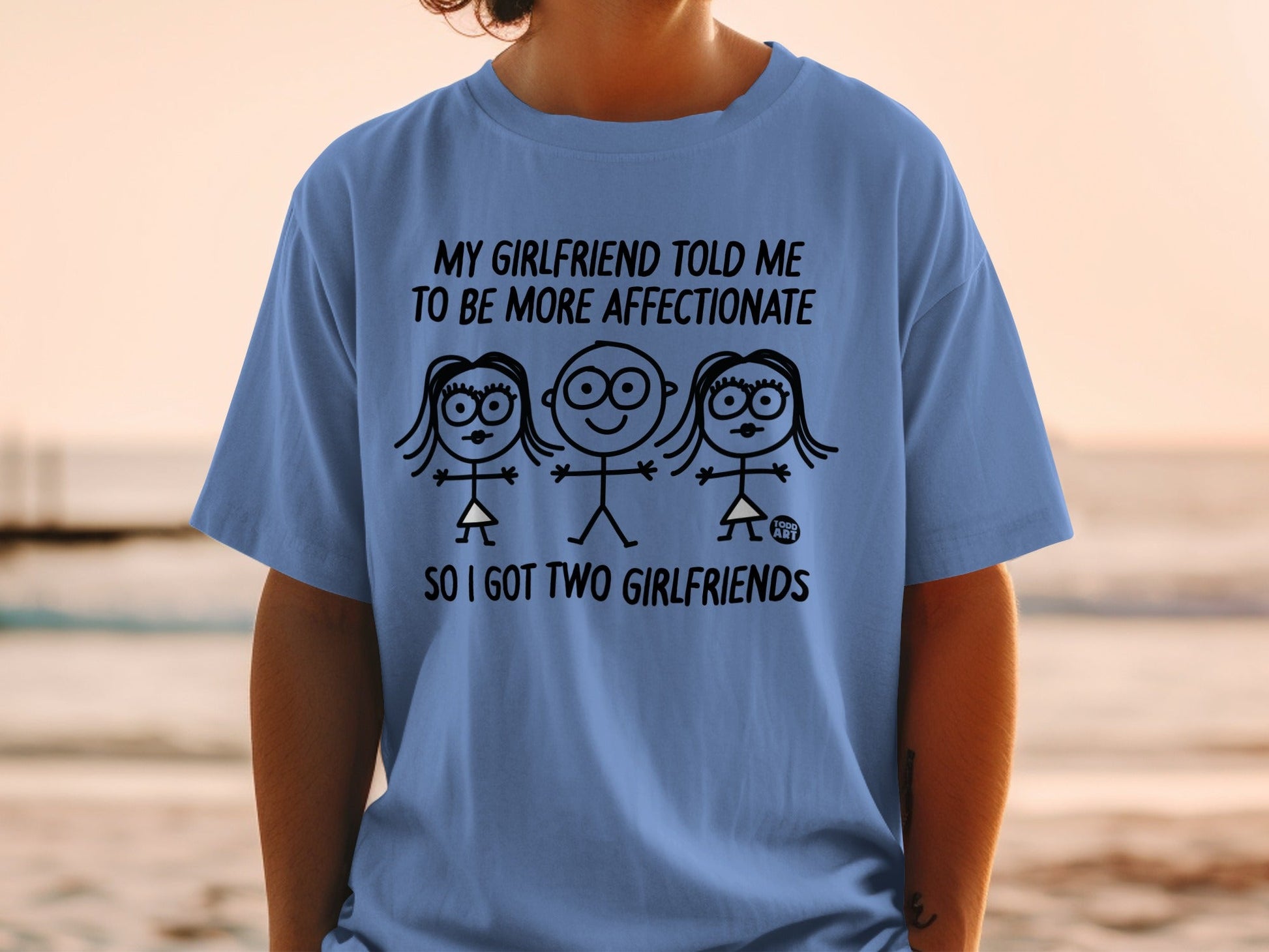 Blue t-shirt with stick figures and text "My girlfriend told me to be more affectionate so I got two girlfriends."