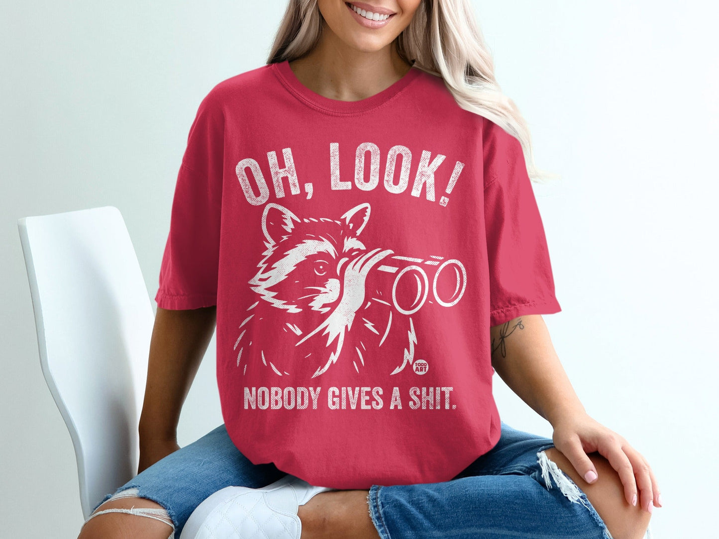 Red t-shirt with raccoon looking through binoculars and text "OH, LOOK! NOBODY GIVES A SHIT."