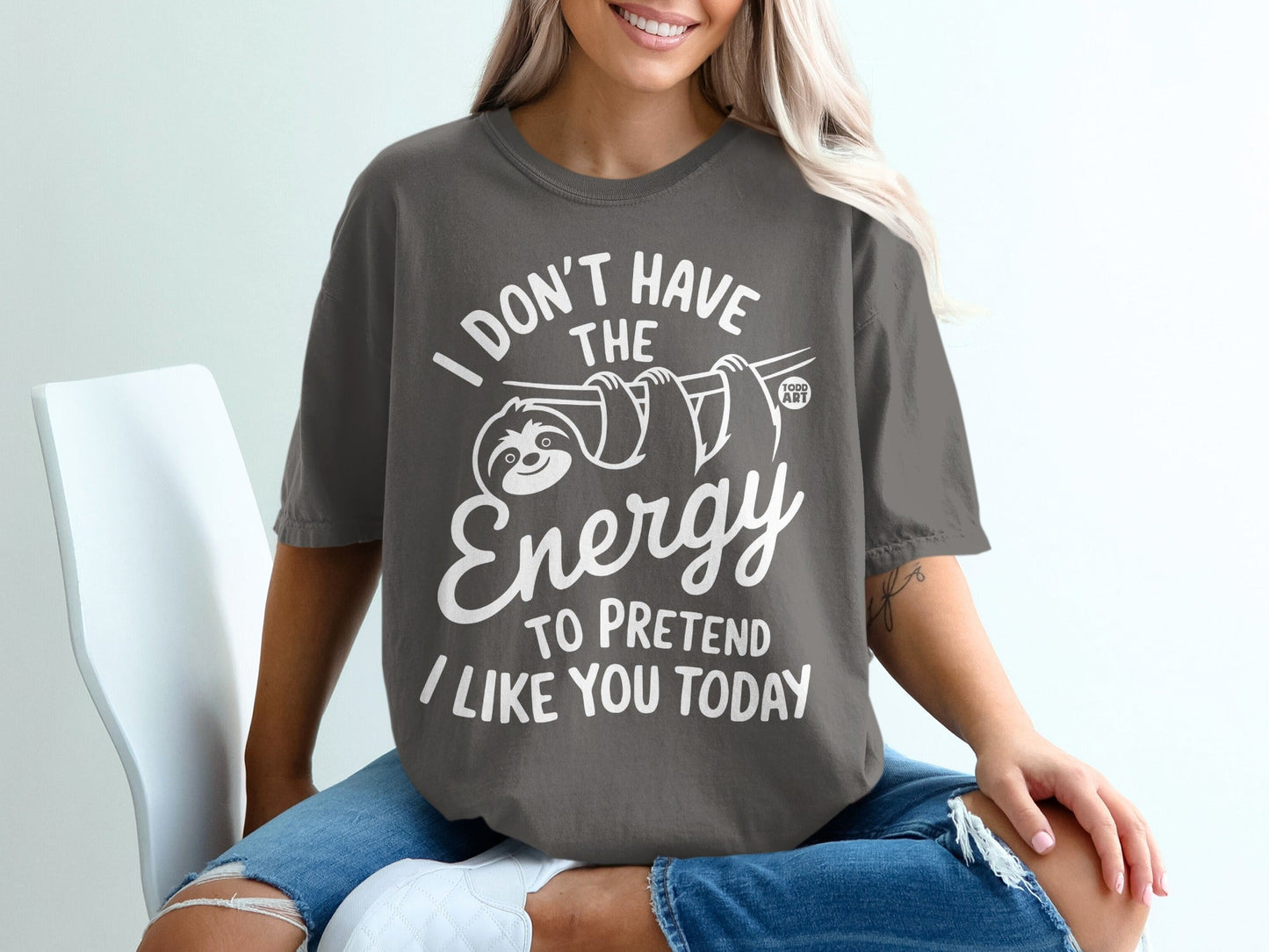 Dark grey t-shirt with white text and a sloth graphic: "I DON'T HAVE THE ENERGY TO PRETEND I LIKE YOU TODAY".