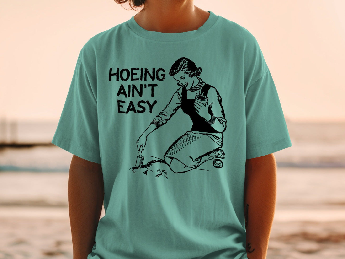 T-shirt with graphic of woman gardening, text "Hoeing Ain't Easy".