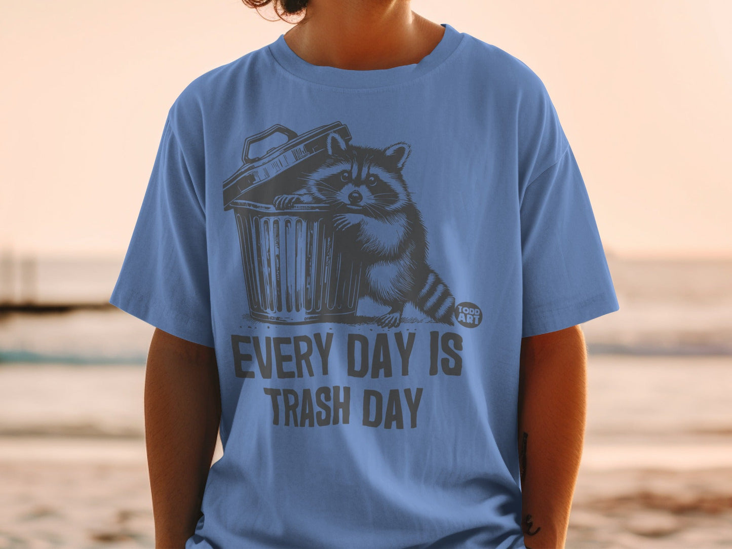 T-shirt with raccoon peeking out of trash can, text reads "EVERY DAY IS TRASH DAY".