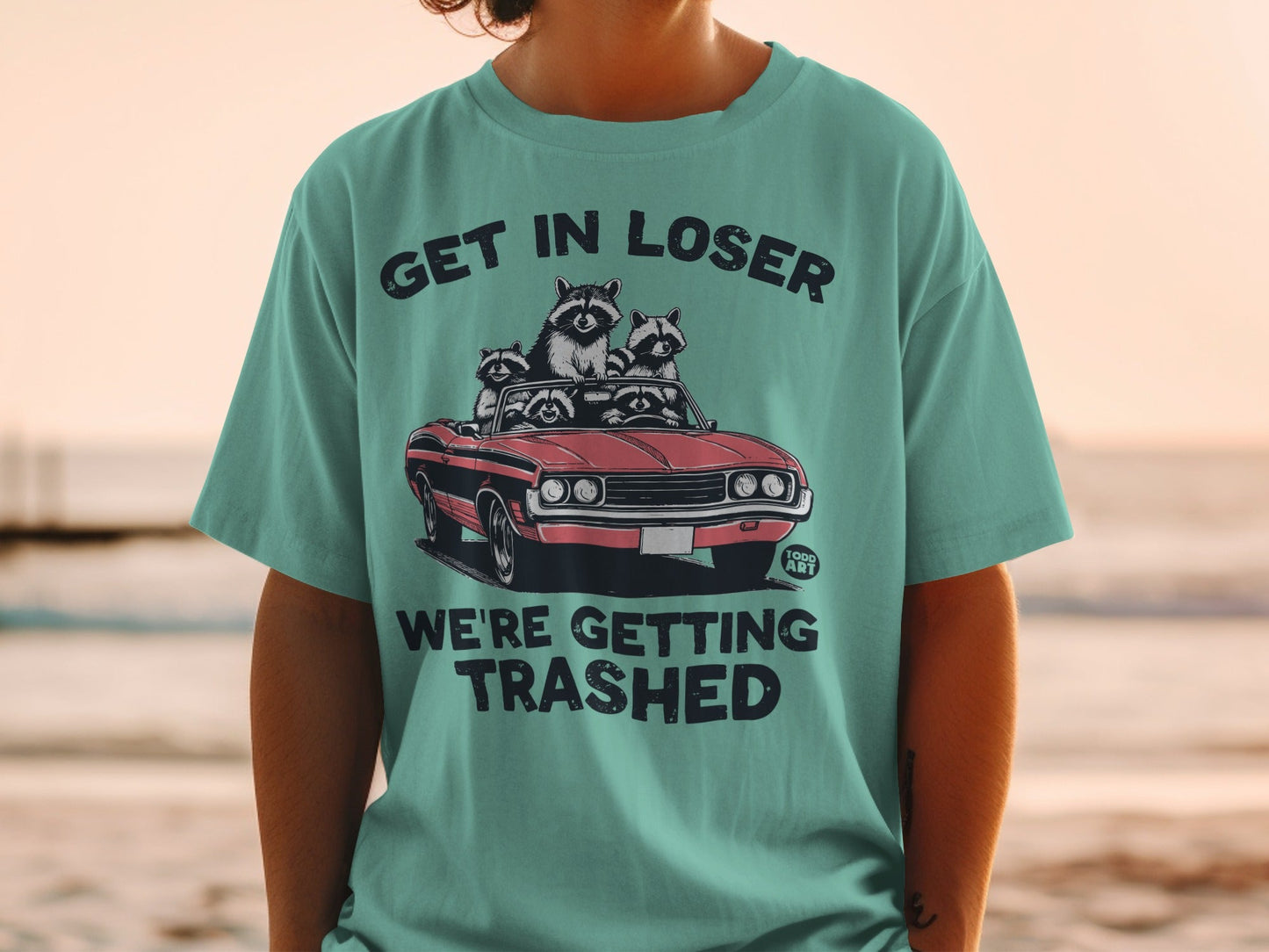 T-shirt with graphic of raccoons in a car with text "GET IN LOSER WE'RE GETTING TRASHED".