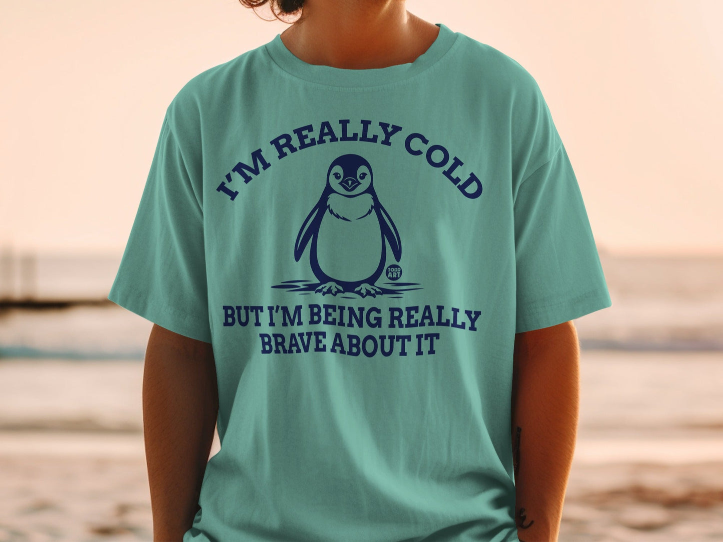 Teal t-shirt with penguin graphic and text "I'm really cold but I'm being really brave about it."