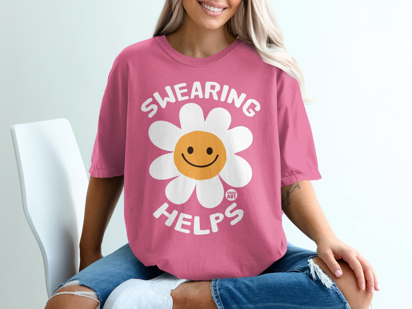 Pink t-shirt with a smiling daisy graphic and "Swearing Helps" text.