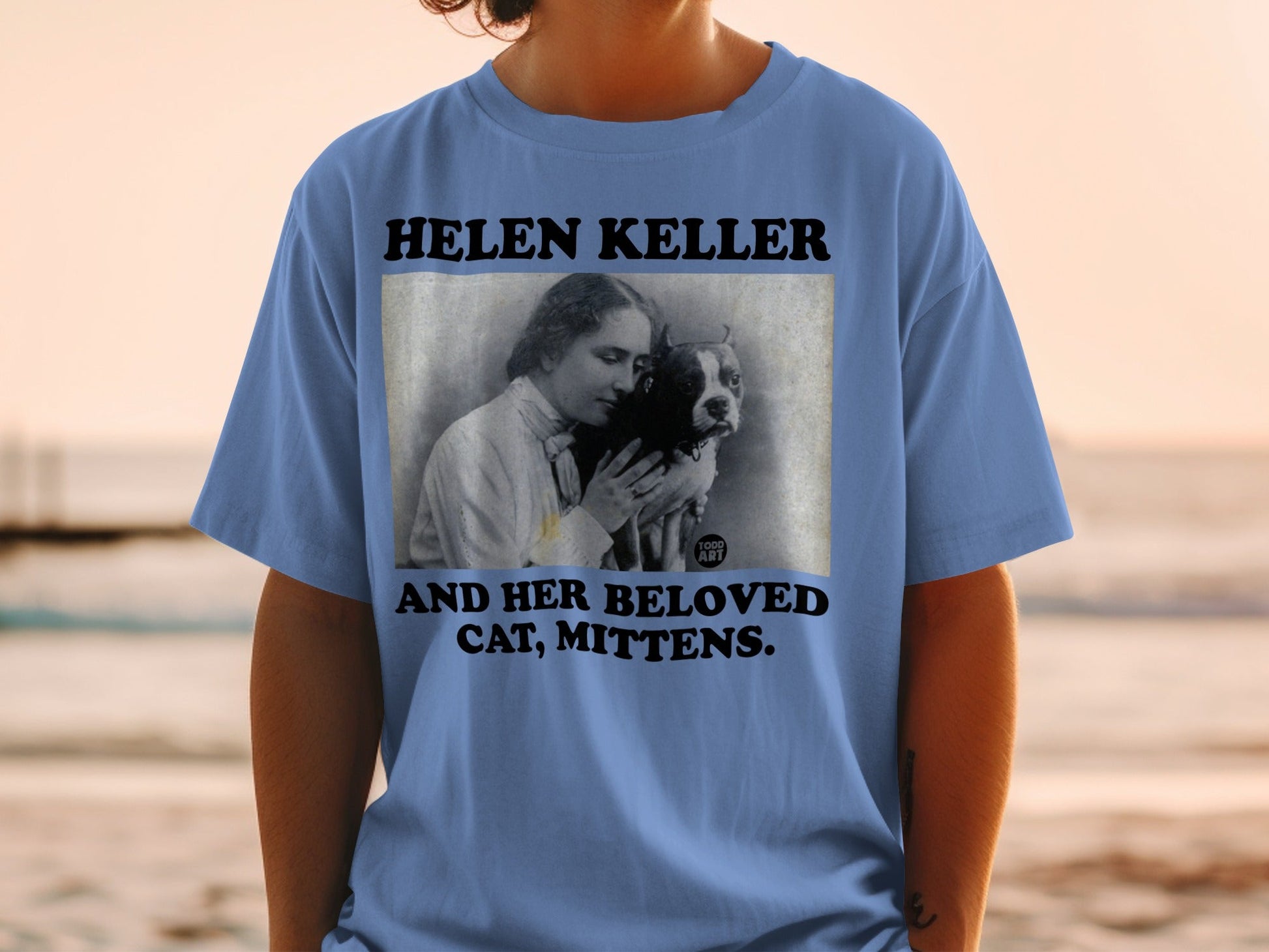 Blue t-shirt with "HELEN KELLER AND HER BELOVED MITTENS" text and a photo.