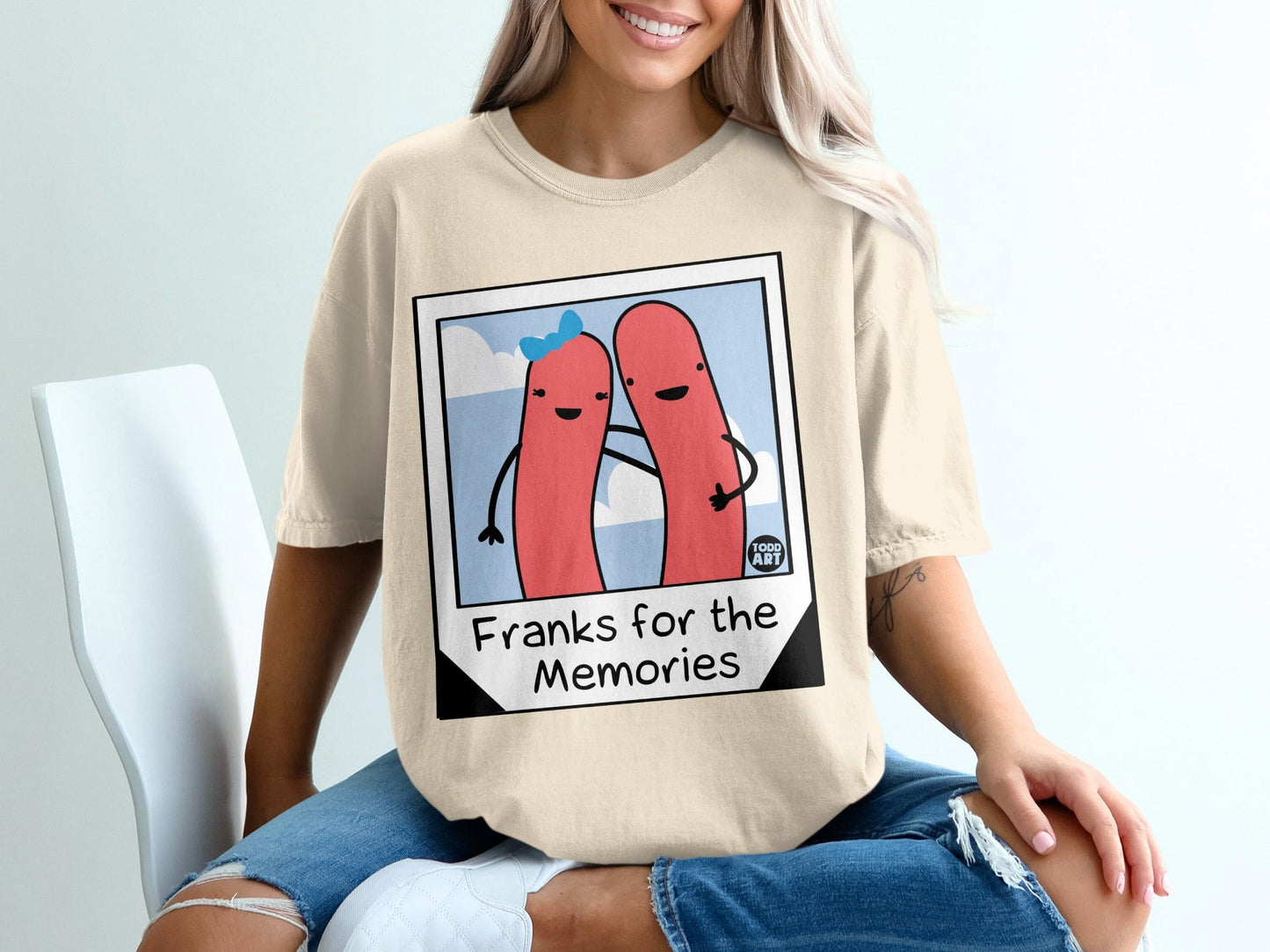 Two cartoon hot dogs embrace on a tan t-shirt with "Franks for the Memories" text.