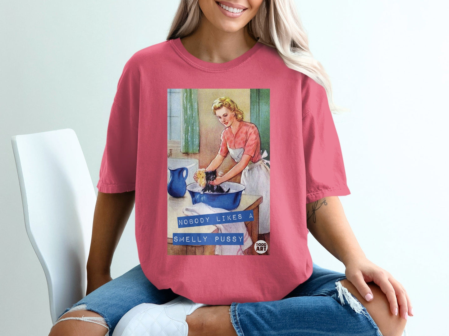 Woman in pink t-shirt showing graphic of retro woman washing cat.