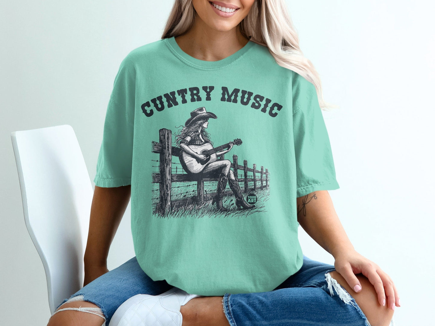 Woman in teal t-shirt with "CUNTry Music" text and graphic.