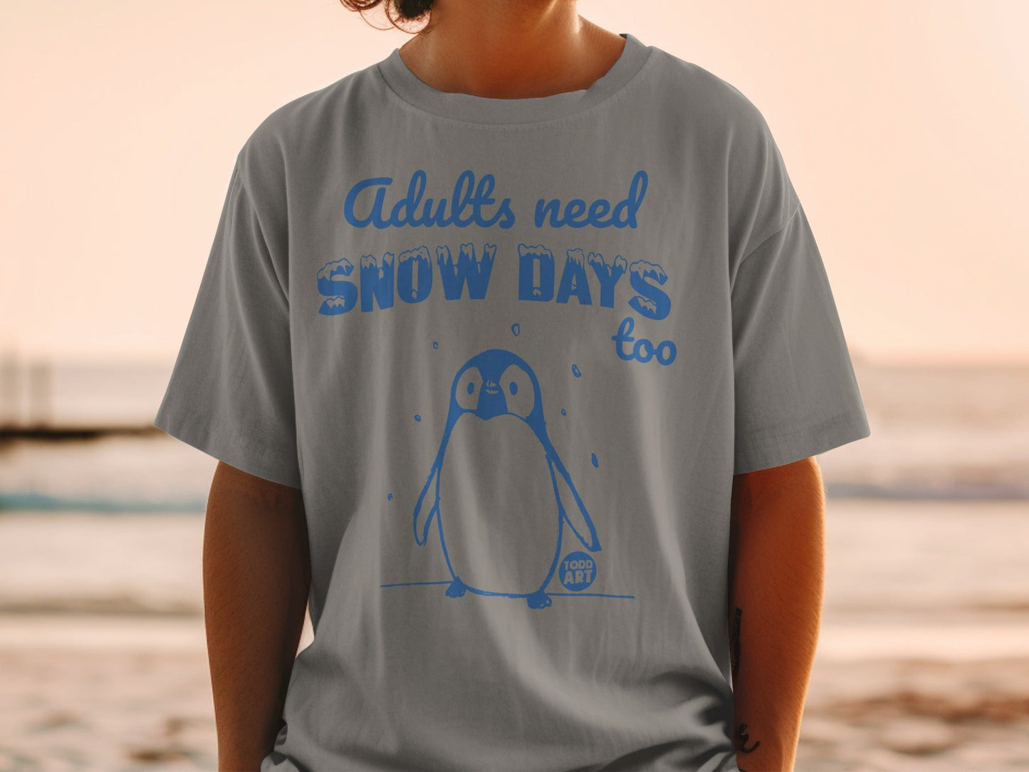 Grey t-shirt with a penguin and the text "Adults need snow days too".