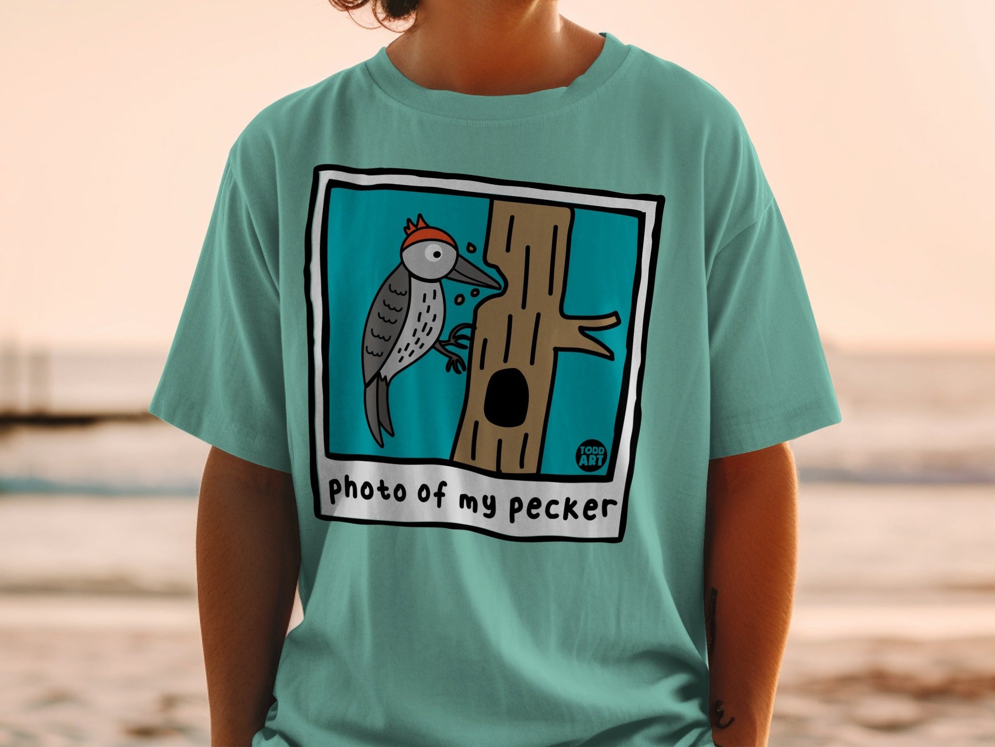 Teal t-shirt with cartoon woodpecker on a tree, "photo of my pecker" text.