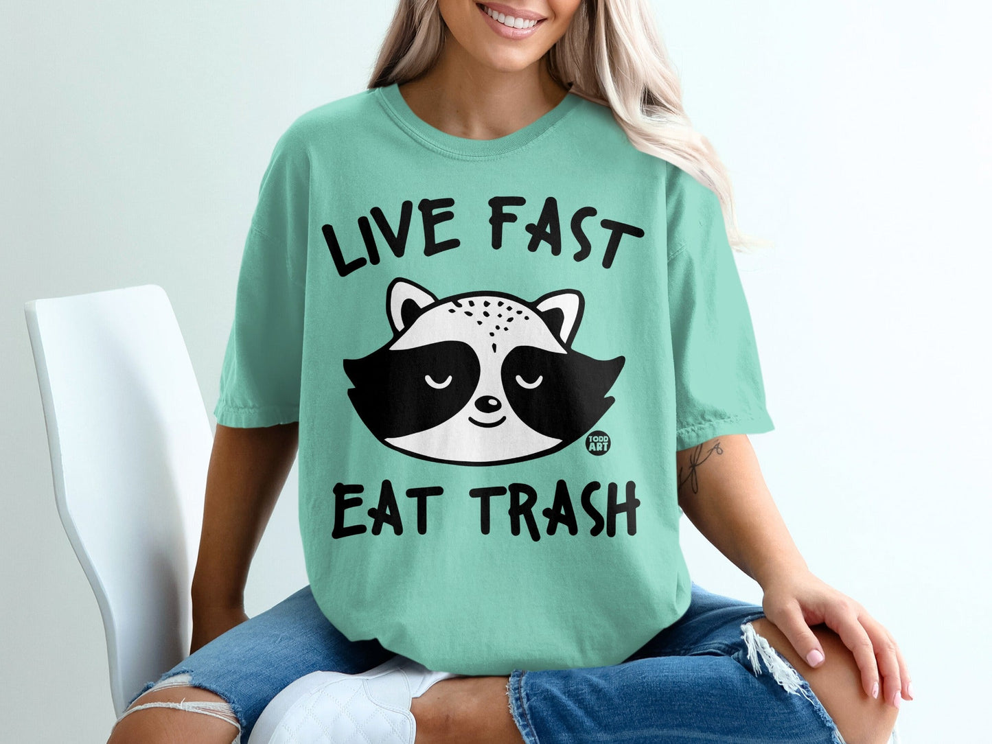 Teal t-shirt with black text "LIVE FAST EAT TRASH" and a raccoon graphic.
