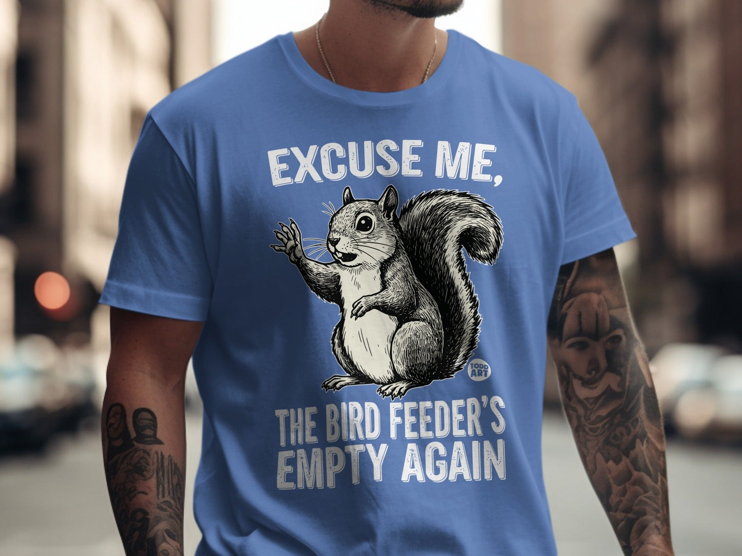 Squirrel on blue t-shirt with "EXCUSE ME, THE BIRD FEEDER'S EMPTY AGAIN" text.