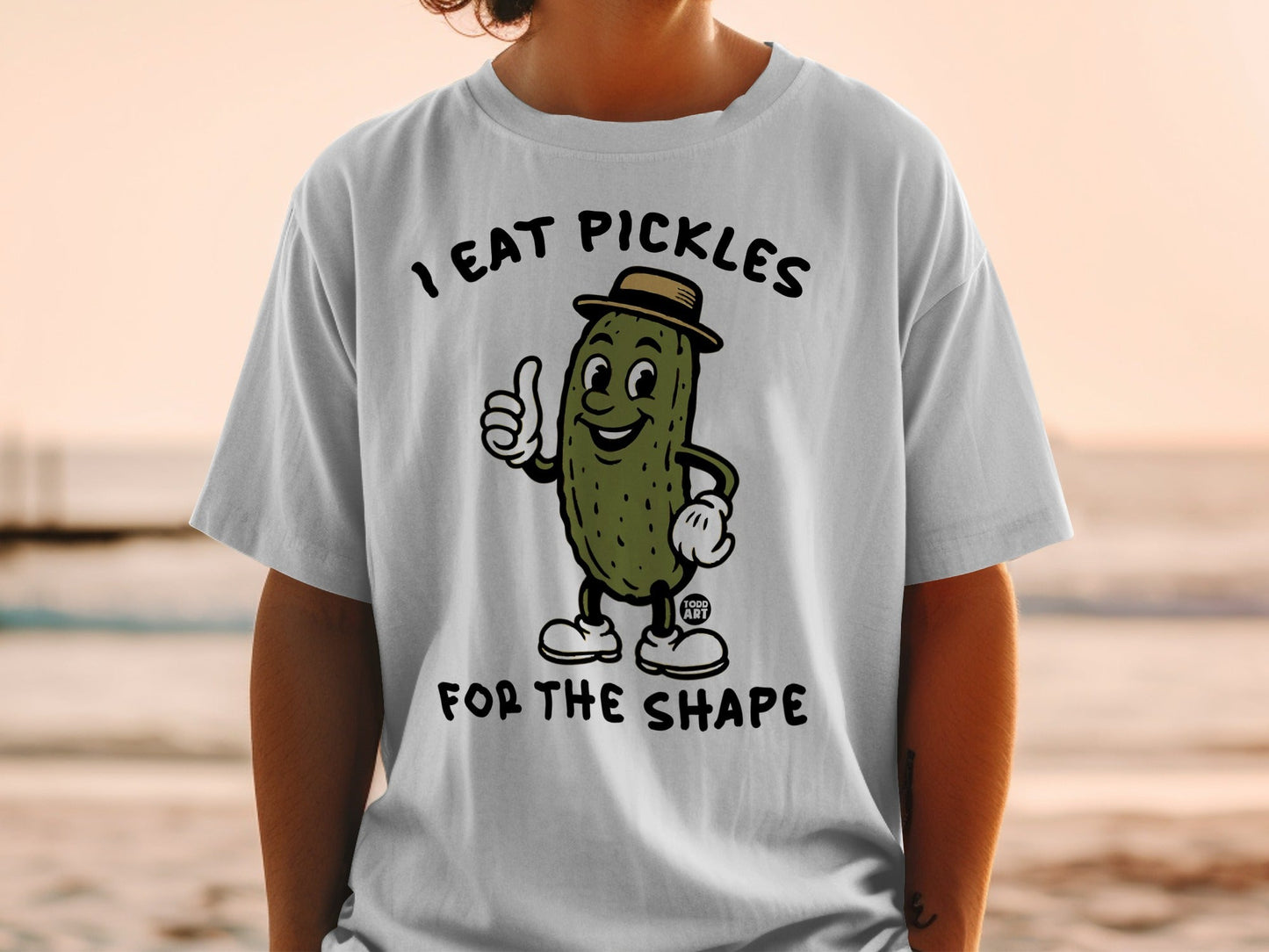 White t-shirt with cartoon pickle giving thumbs up, text "I EAT PICKLES FOR THE SHAPE".