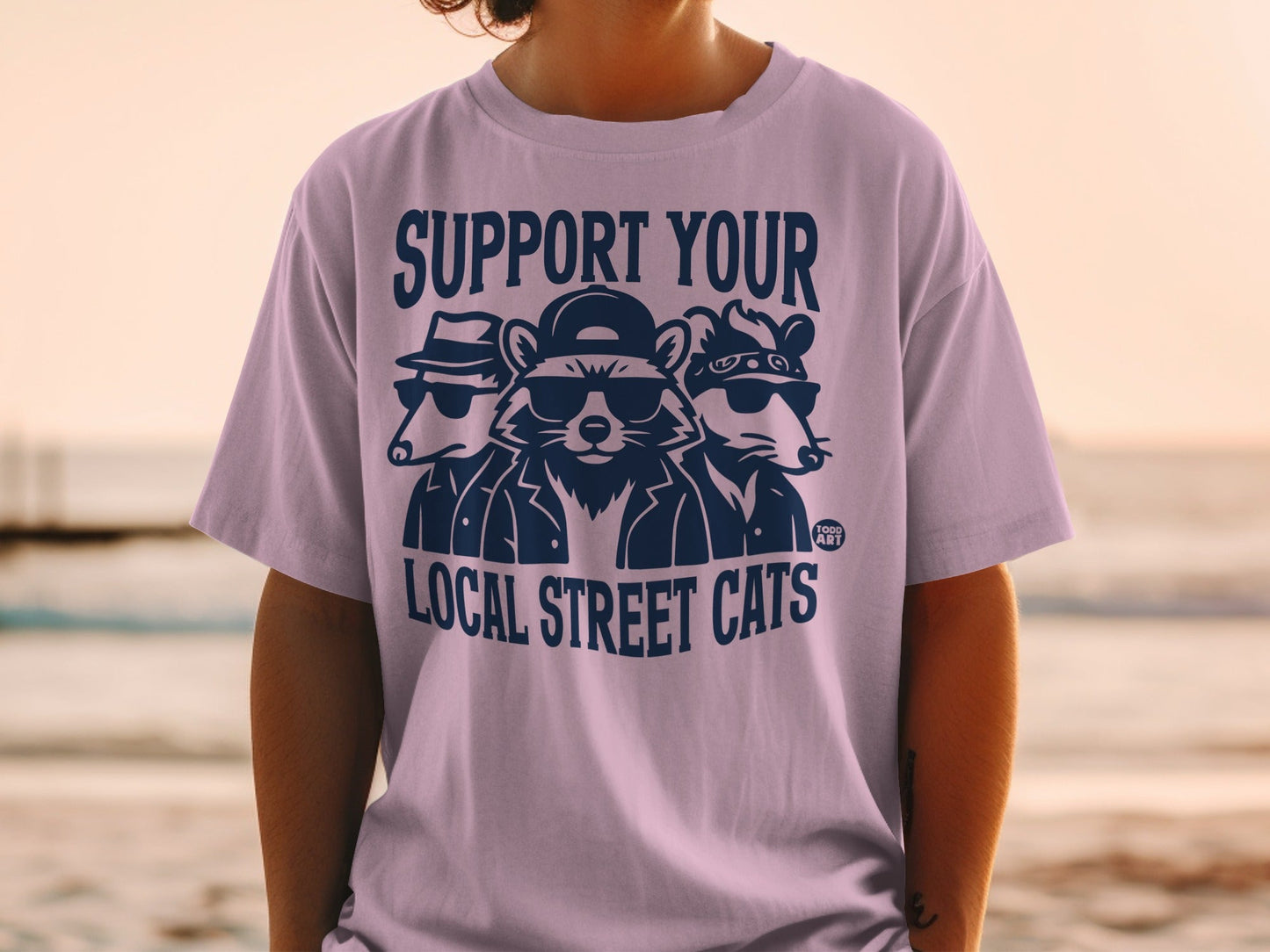 T-shirt with graphic of three cartoon raccoons wearing sunglasses and hats.