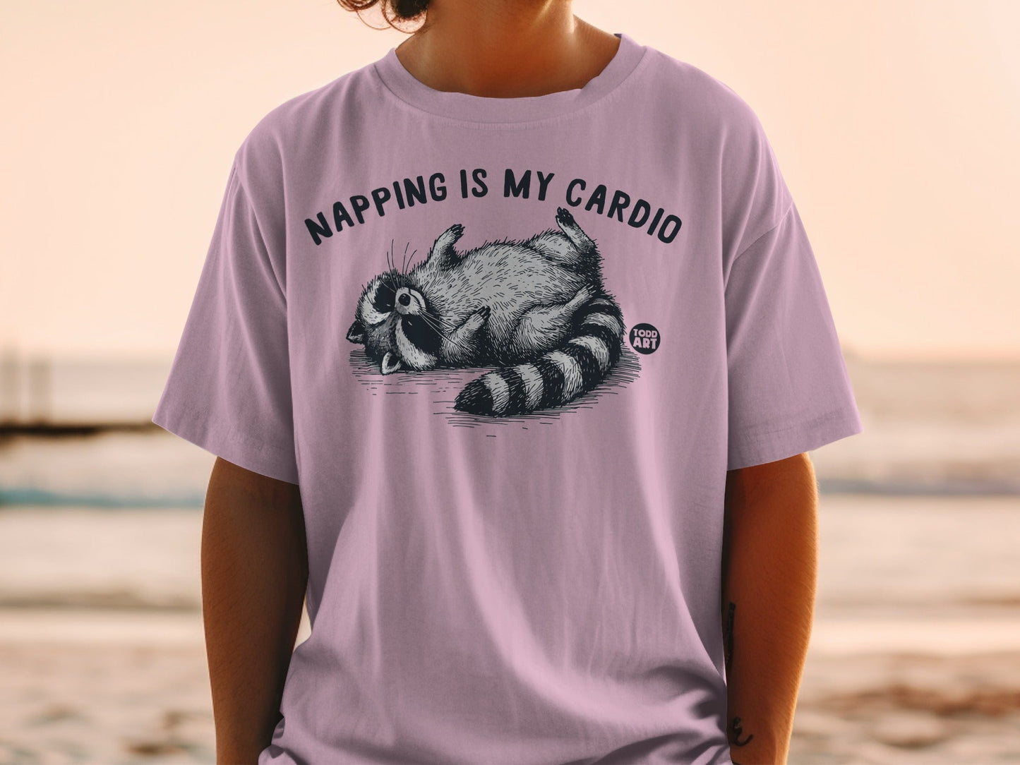 T-shirt with a raccoon lying on its back, text reads "NAPPING IS MY CARDIO".