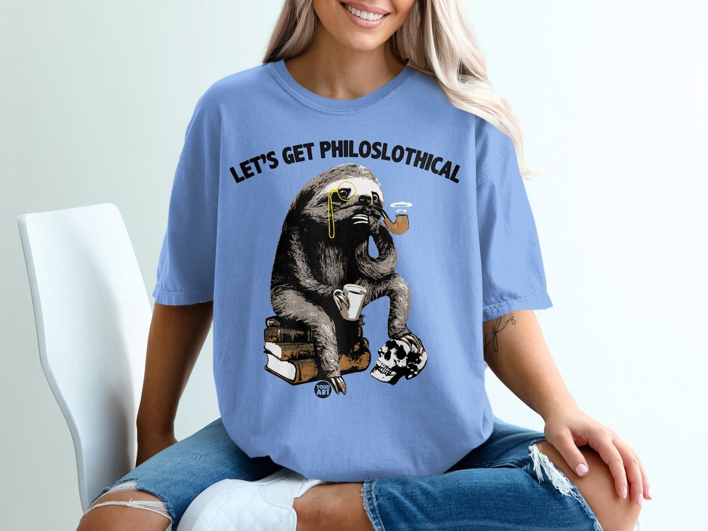 Sloth in monocle and pipe sits on books with skull, text "LET'S GET PHILOSLOTHICAL".