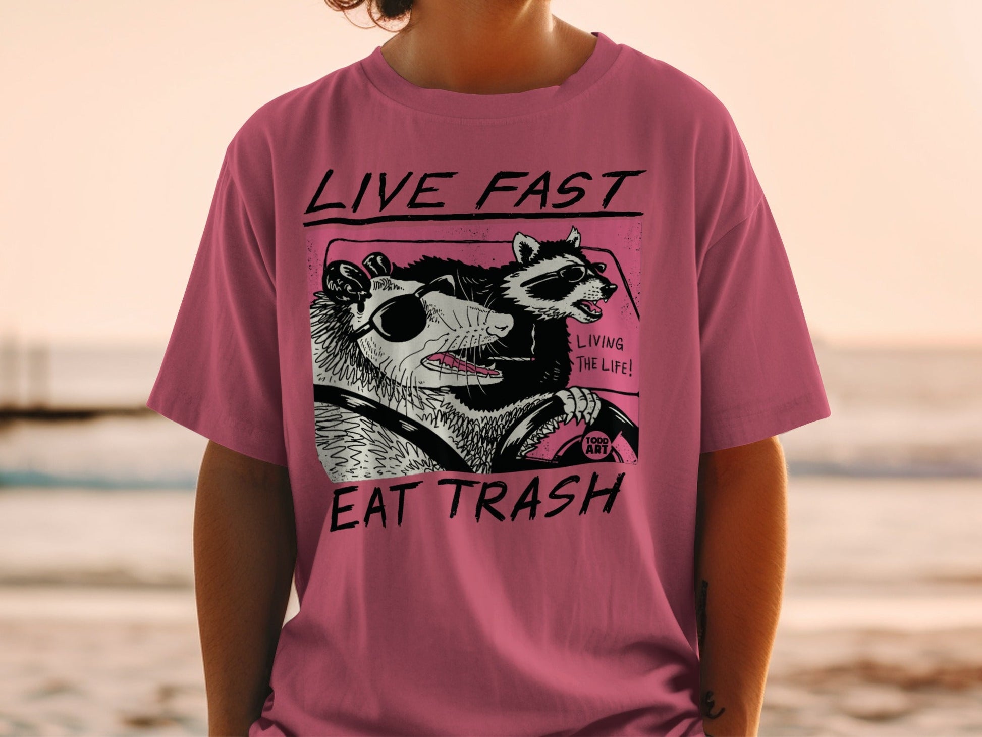 T-shirt with possum and raccoon driving, "Live Fast Eat Trash" text.