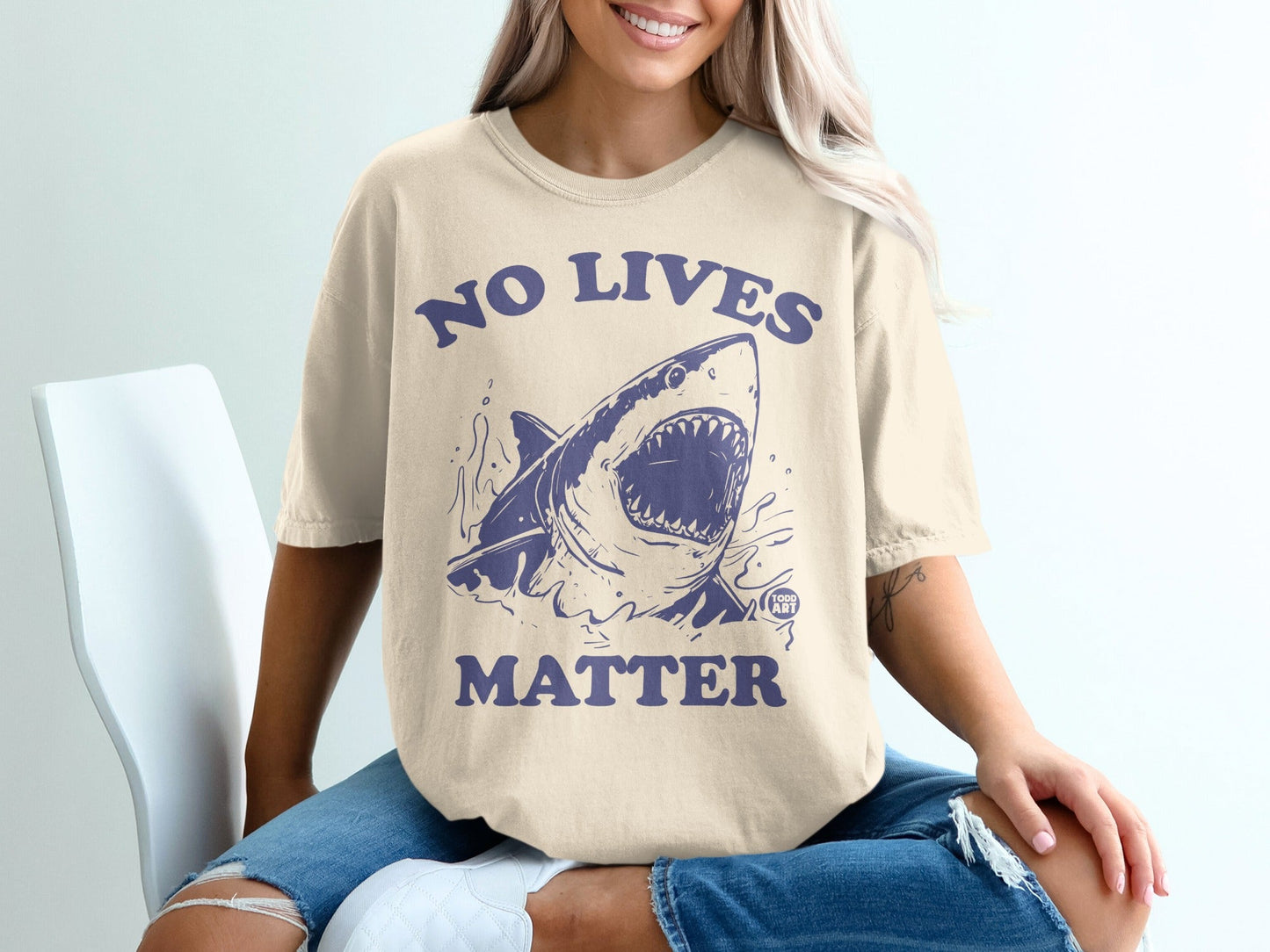Cream t-shirt with navy graphic of a shark and text "NO LIVES MATTER".