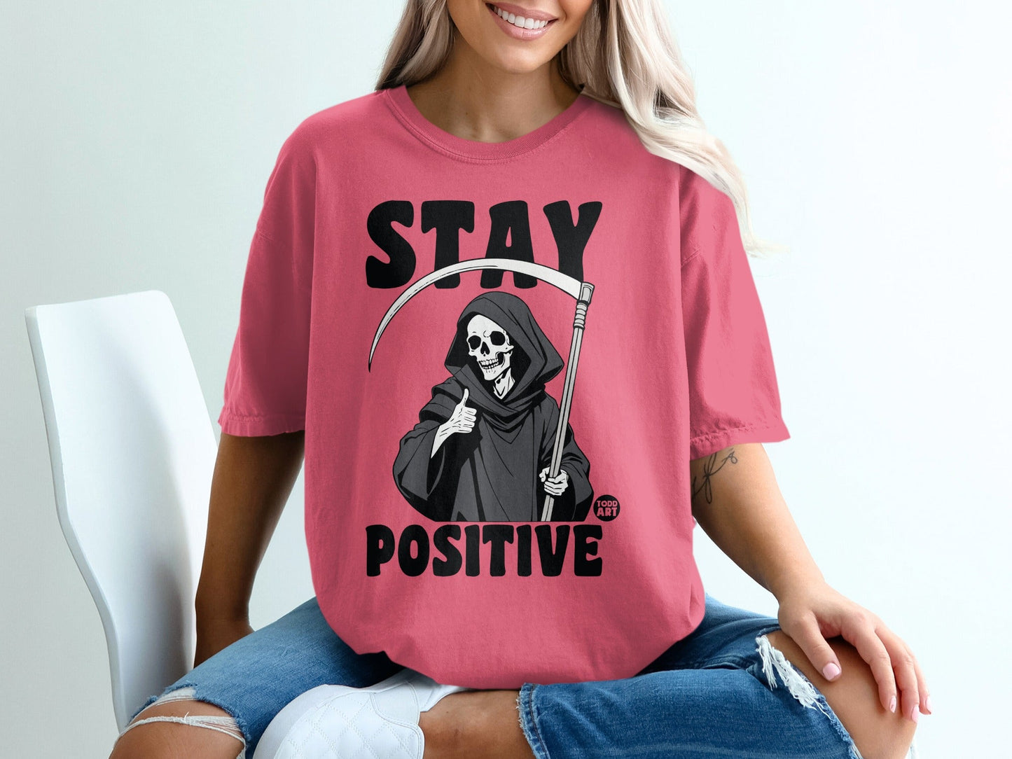 Pink t-shirt with Grim Reaper giving thumbs up and text "STAY POSITIVE"