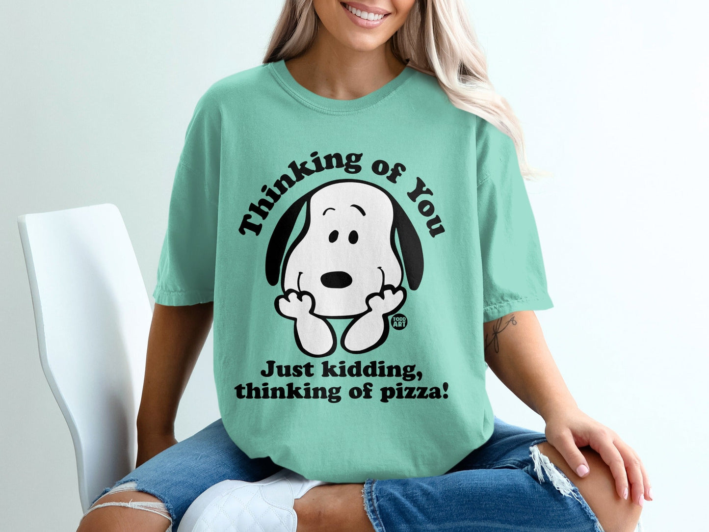 Snoopy the dog wearing a t-shirt that says "Thinking of you. Just kidding, thinking of pizza!".