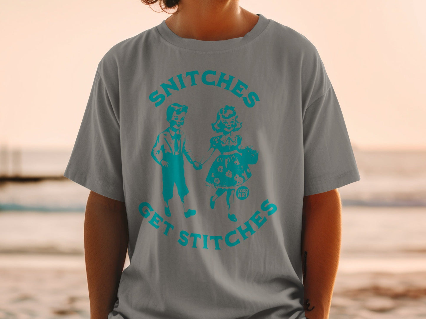 Gray t-shirt with teal graphic of two children and text "SNITCHES GET STITCHES".