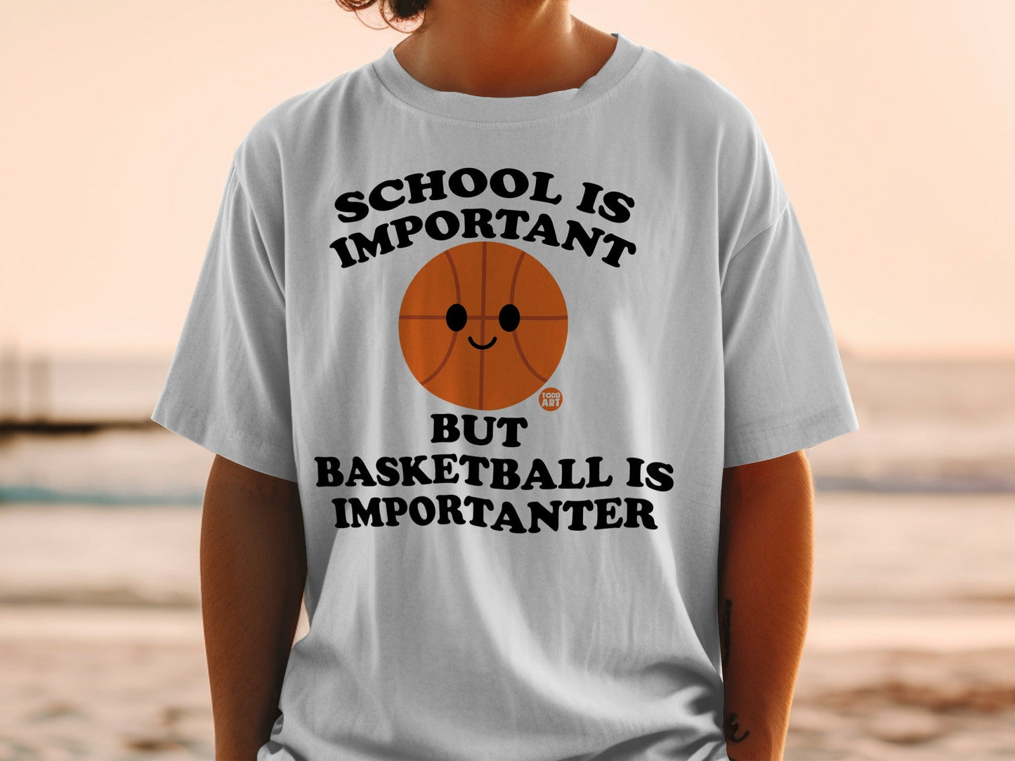 White t-shirt with text "SCHOOL IS IMPORTANT BUT BASKETBALL IS IMPORTANTER" and a basketball graphic.