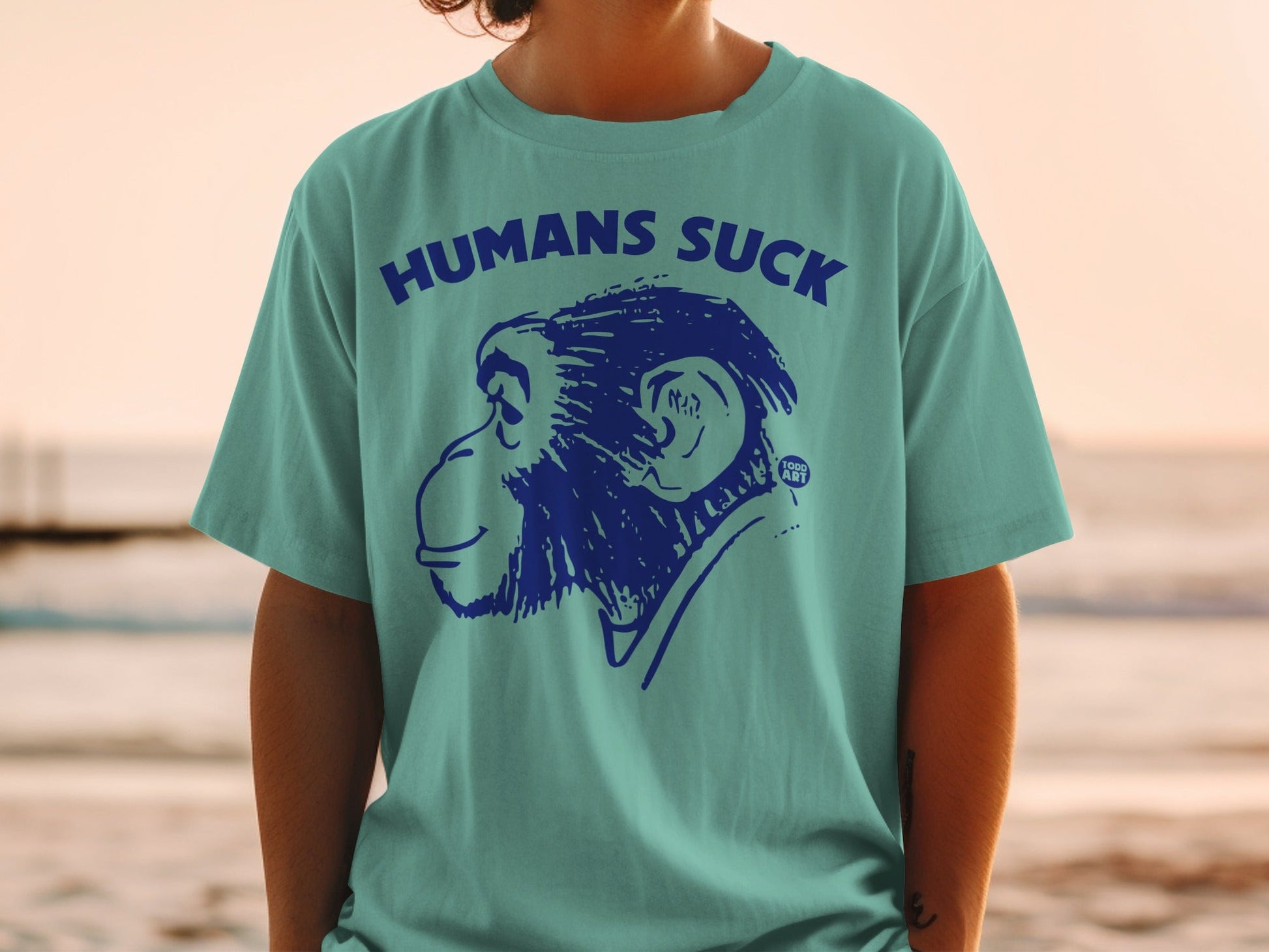 Blue ape graphic with "HUMANS SUCK" text on teal t-shirt.