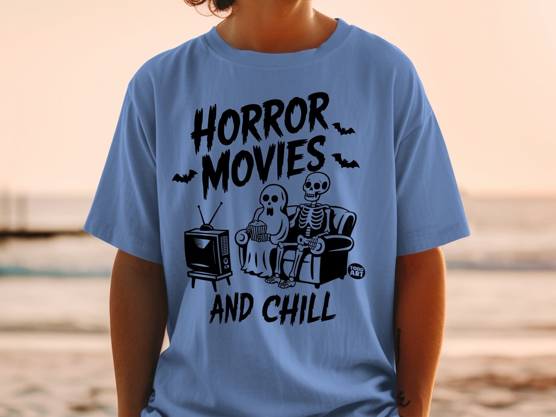 Blue t-shirt with "Horror Movies And Chill" text, skeletons, and a TV.