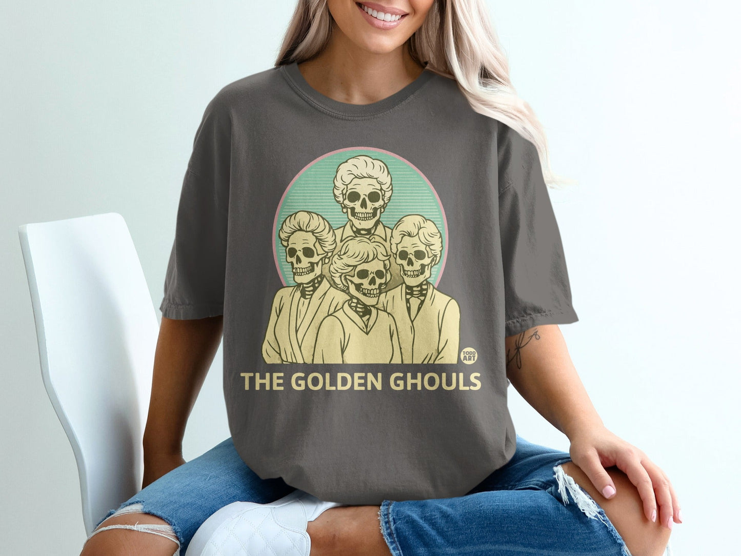 Dark gray t-shirt with "The Golden Ghouls" in yellow text above a circular illustration of four skeletons.