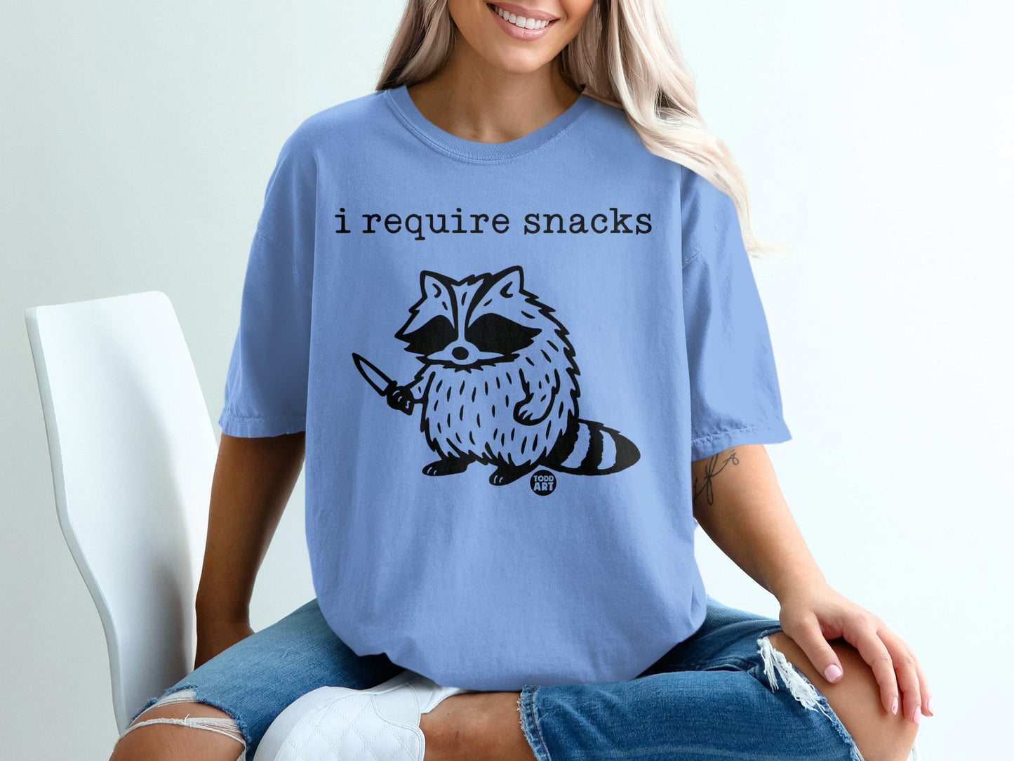T-shirt with raccoon holding knife and text "I require snacks".