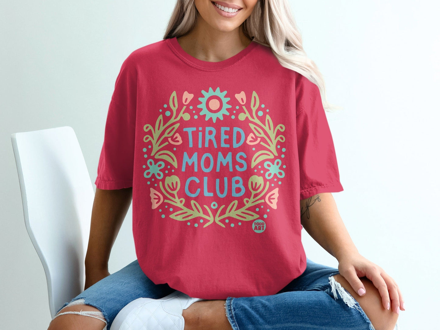 Red t-shirt with "Tired Moms Club" text and floral wreath design.