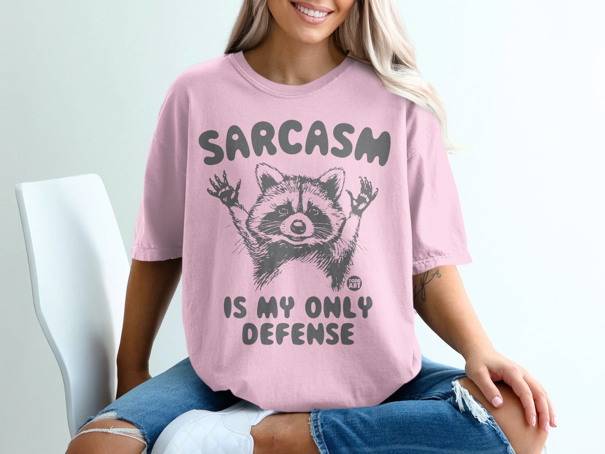 Pink t-shirt with "SARCASM IS MY ONLY DEFENSE" and a raccoon graphic.