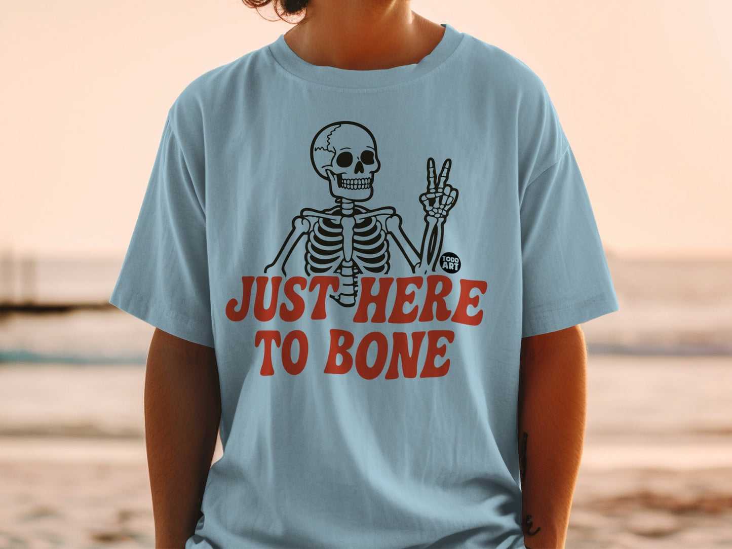 Light blue t-shirt with skeleton graphic and text "JUST HERE TO BONE".