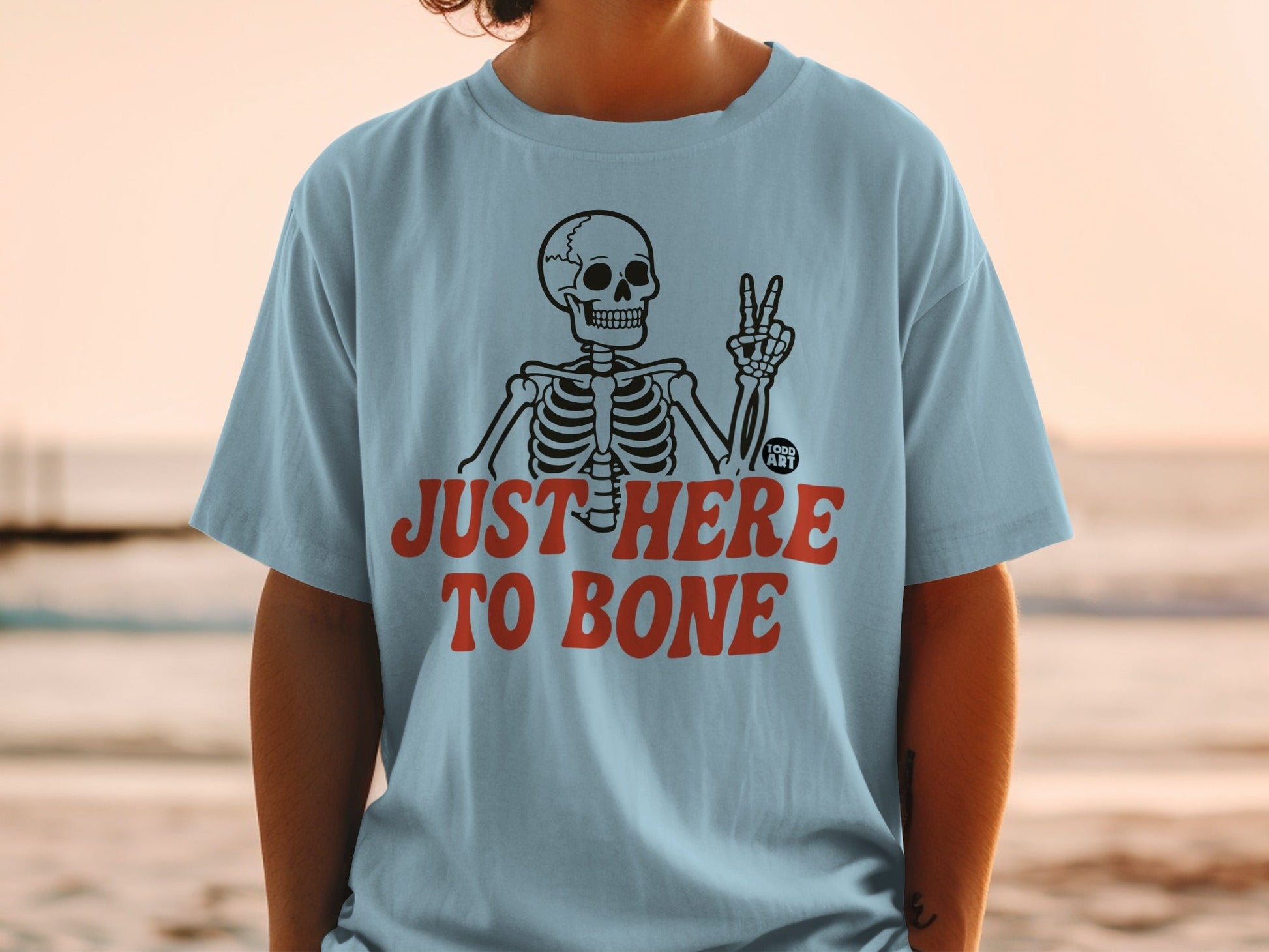 Light blue t-shirt with skeleton graphic and text "JUST HERE TO BONE".