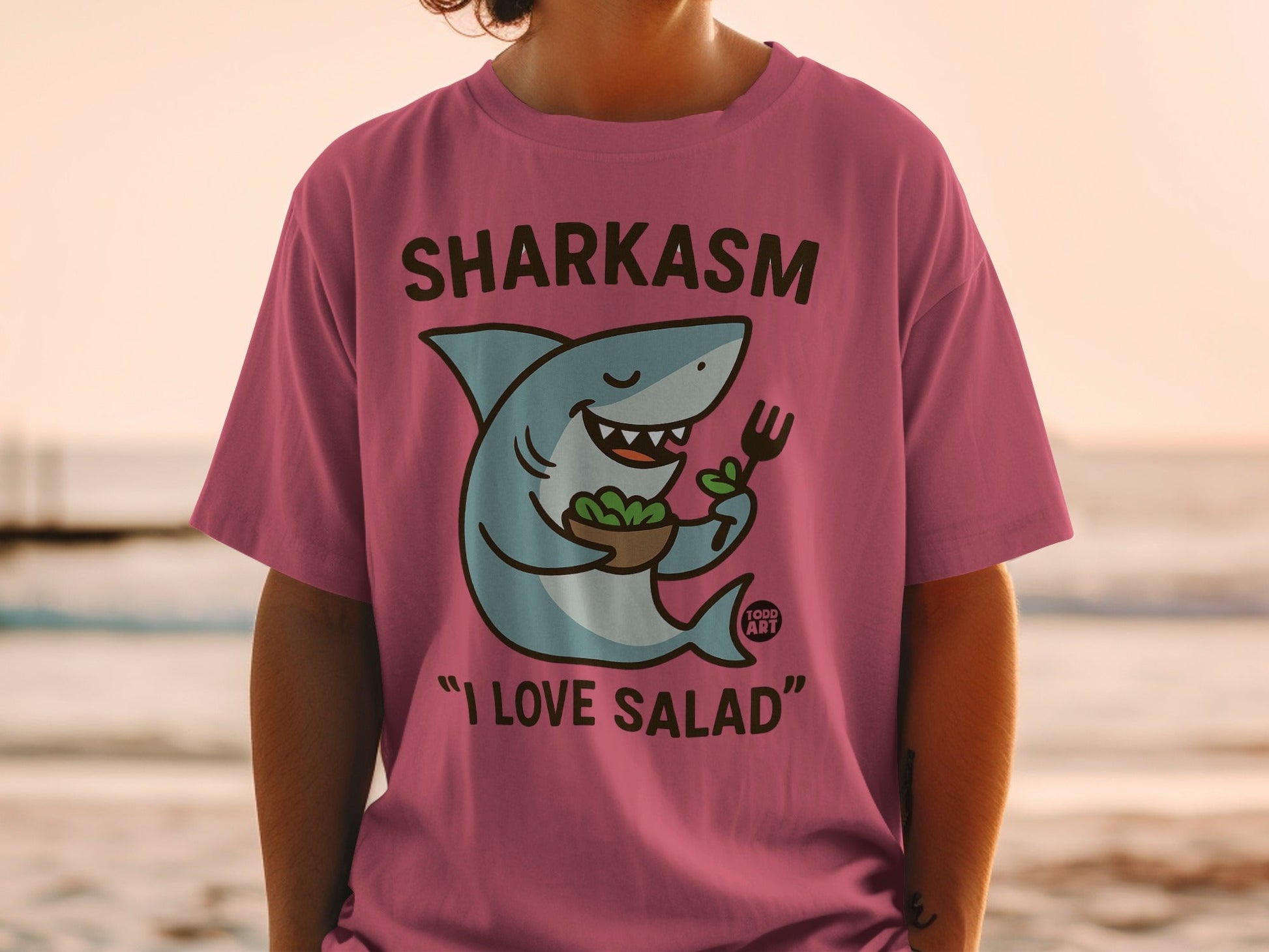 Pink t-shirt with "Sharkasm I Love Salad" text and a shark eating salad.