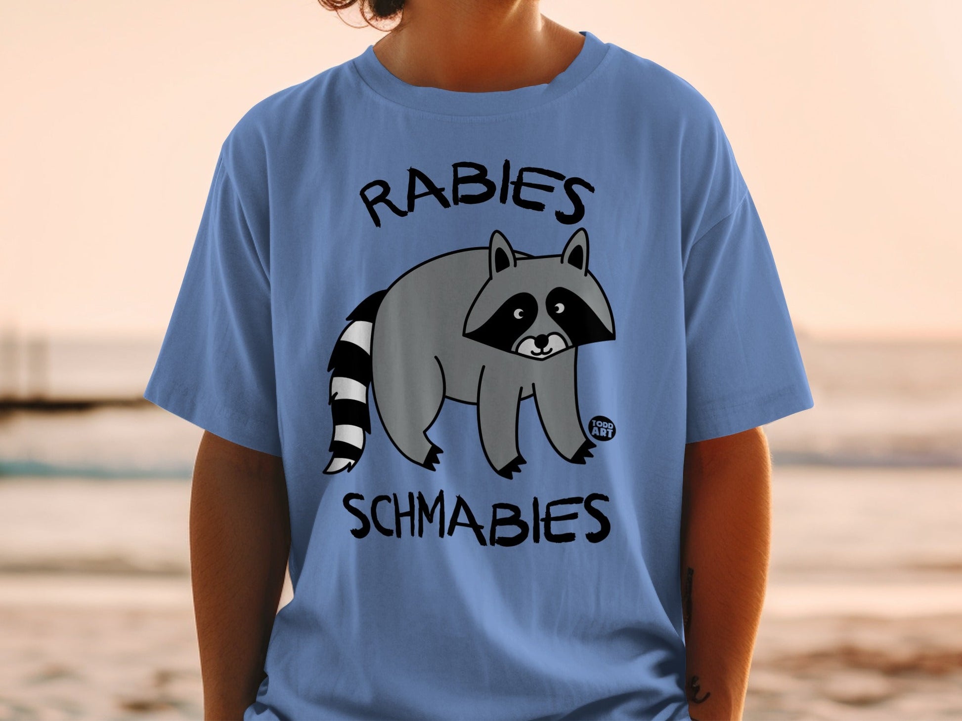 Blue t-shirt with raccoon graphic and text "RABIES SCHMABIES".