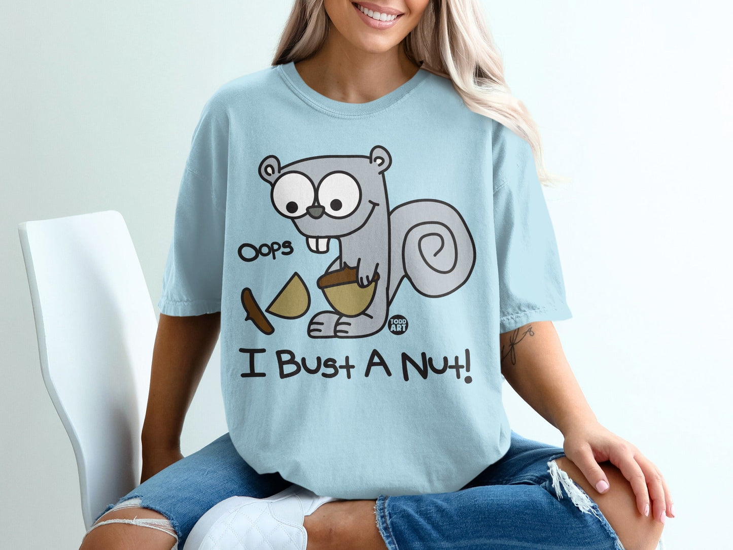 Light blue t-shirt with cartoon squirrel holding a nut and text "Oops I Bust A Nut!".