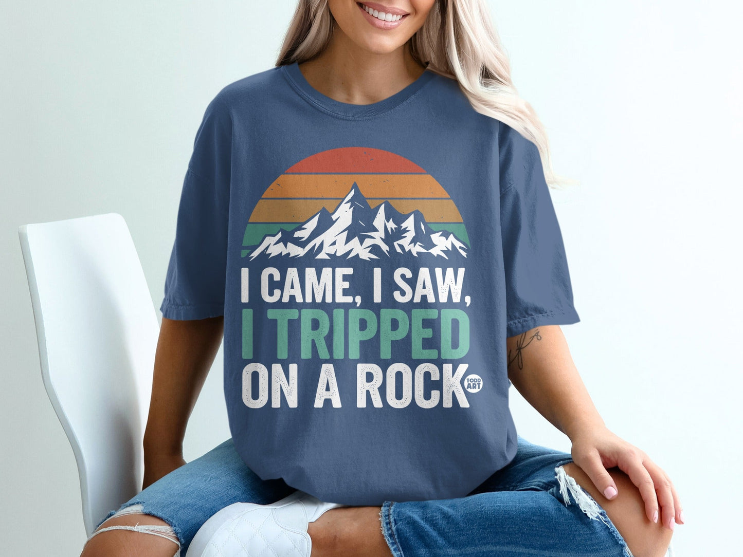 Navy t-shirt with "I came, I saw, I tripped on a rock" and mountain sunset graphic.