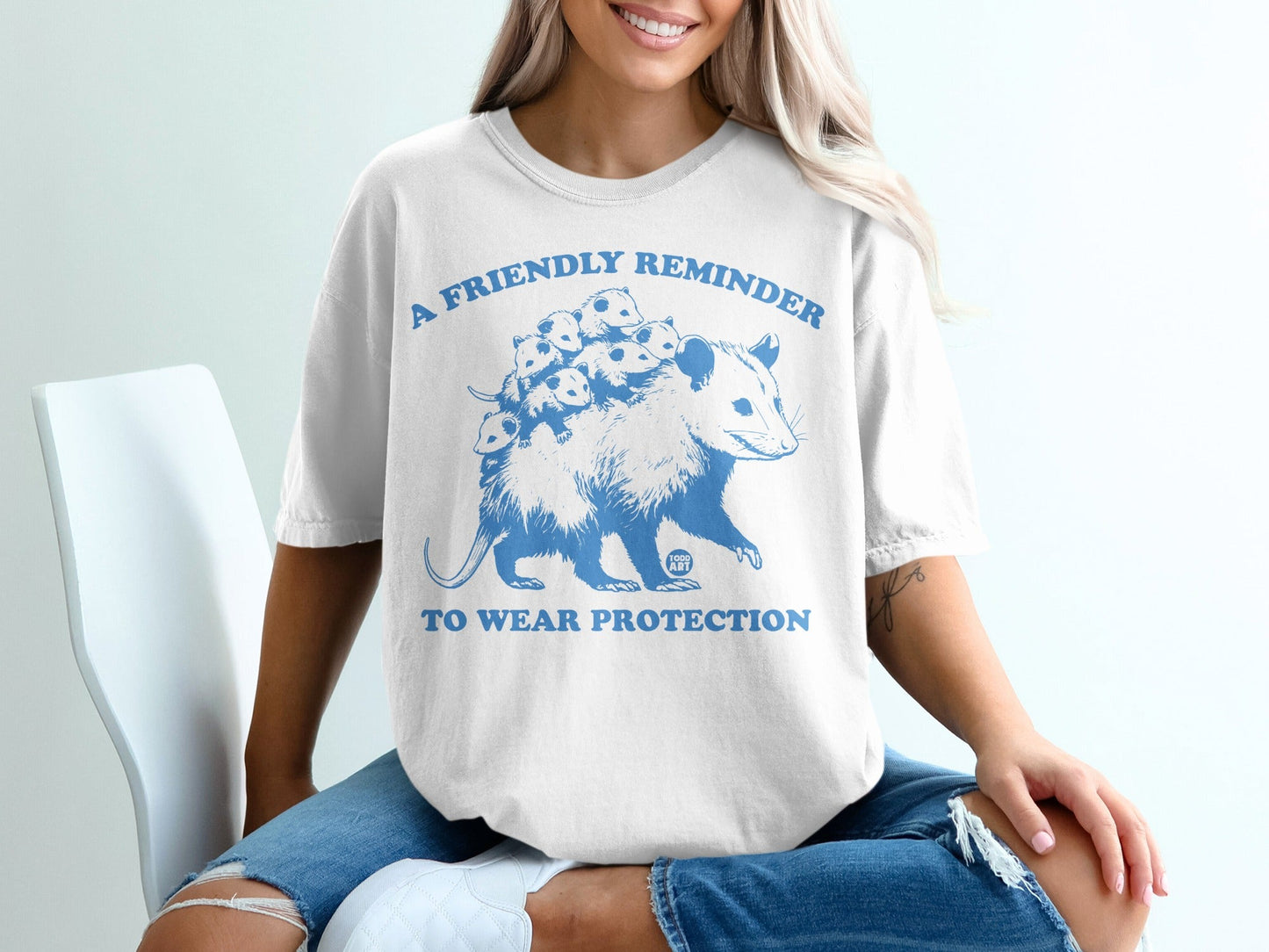 T-shirt with blue graphic of an opossum and babies, text reads "A friendly reminder to wear protection".